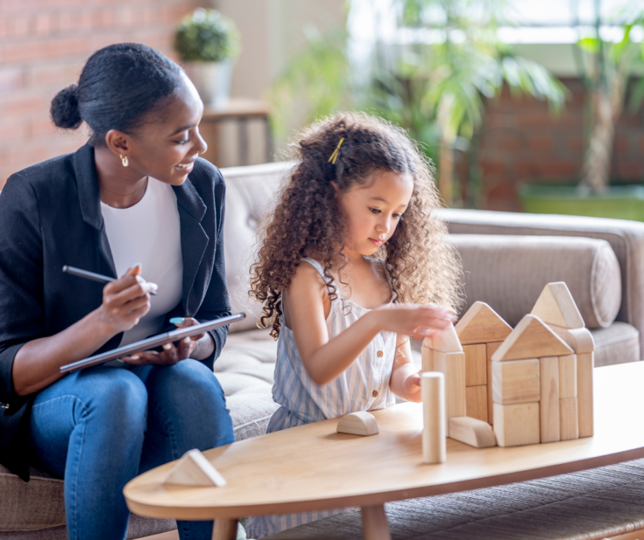 A woman is sitting on a couch talking to a little girl who is playing with wooden blocks.