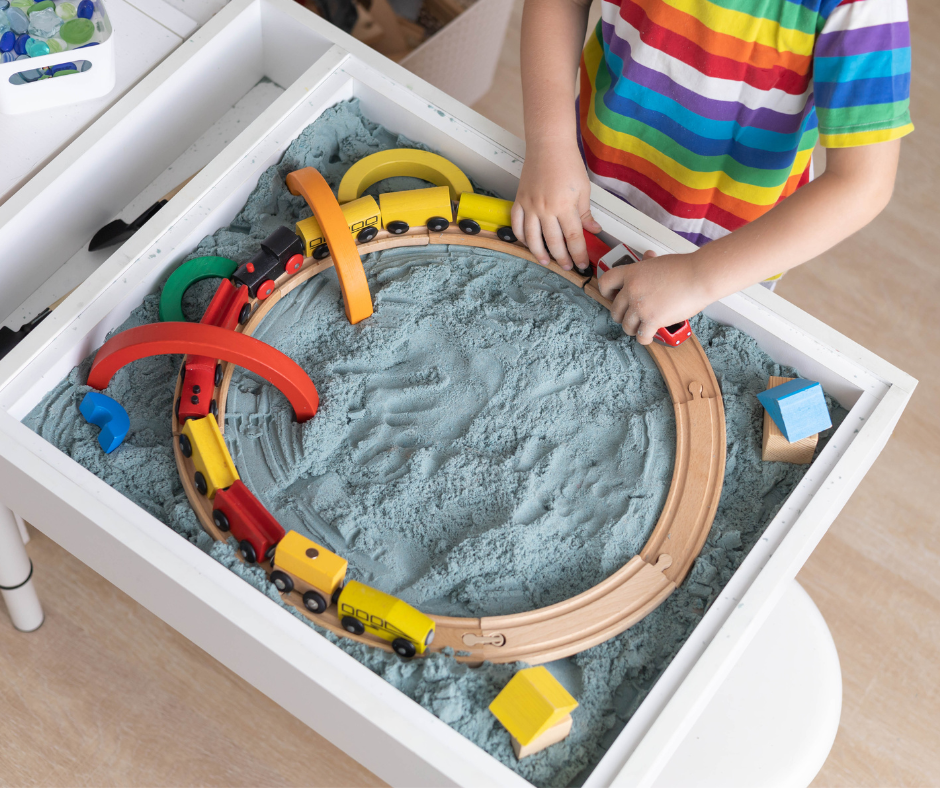 A child is playing with a train set in a sandbox.