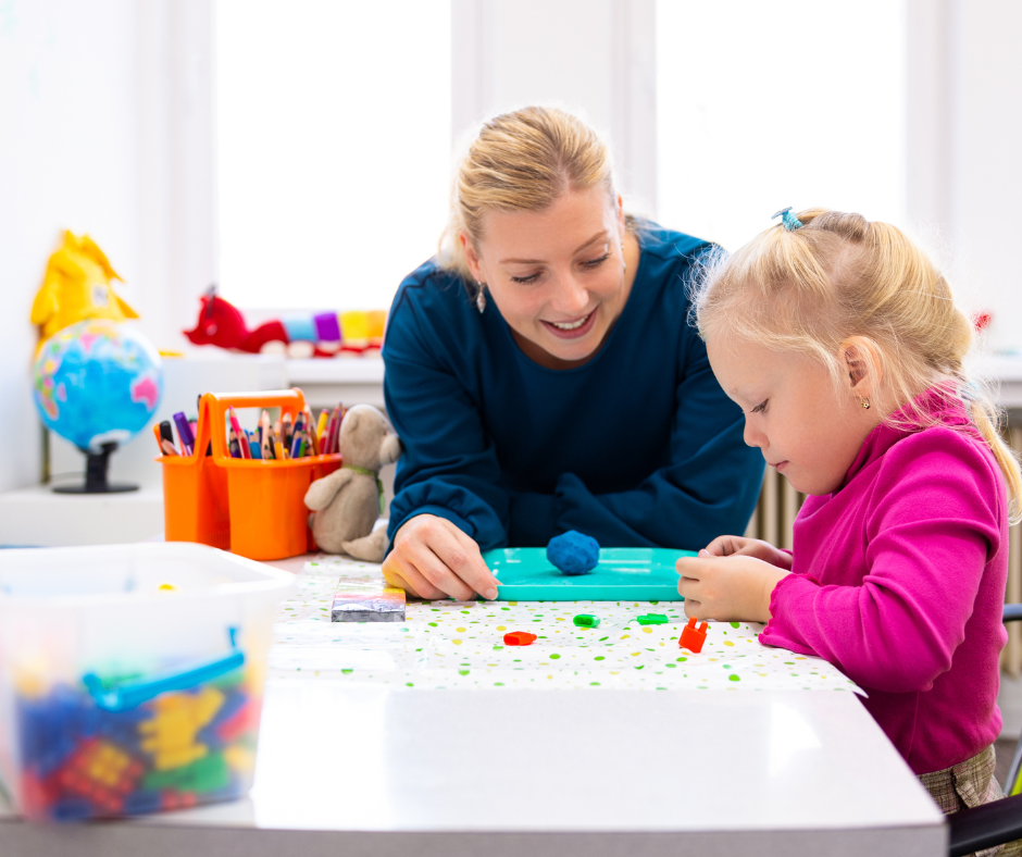 A woman and a little girl are playing with clay at a table.
