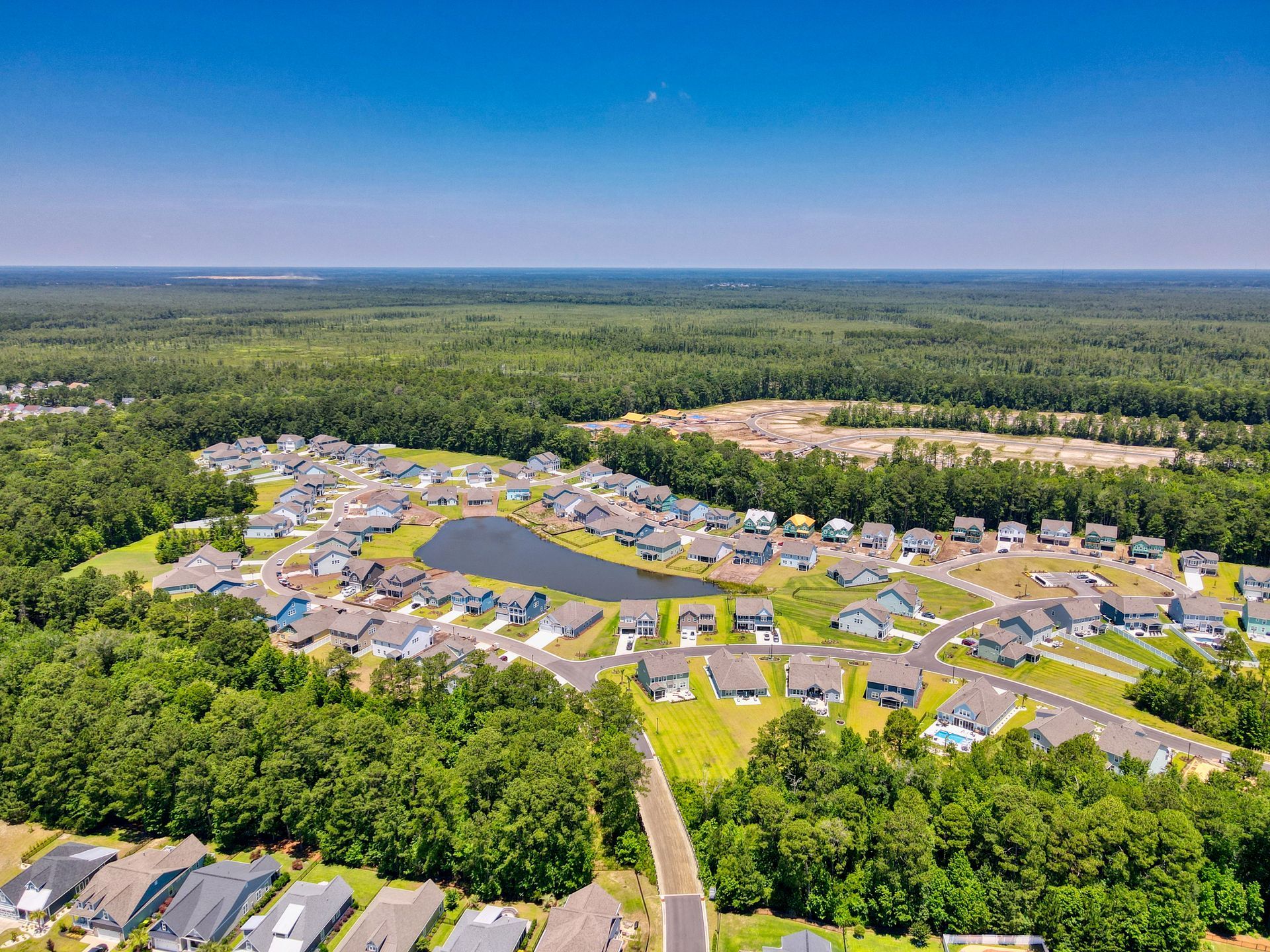 Aerial view of a suburban neighborhood with houses, a lake, and surrounding forest on a sunny day.