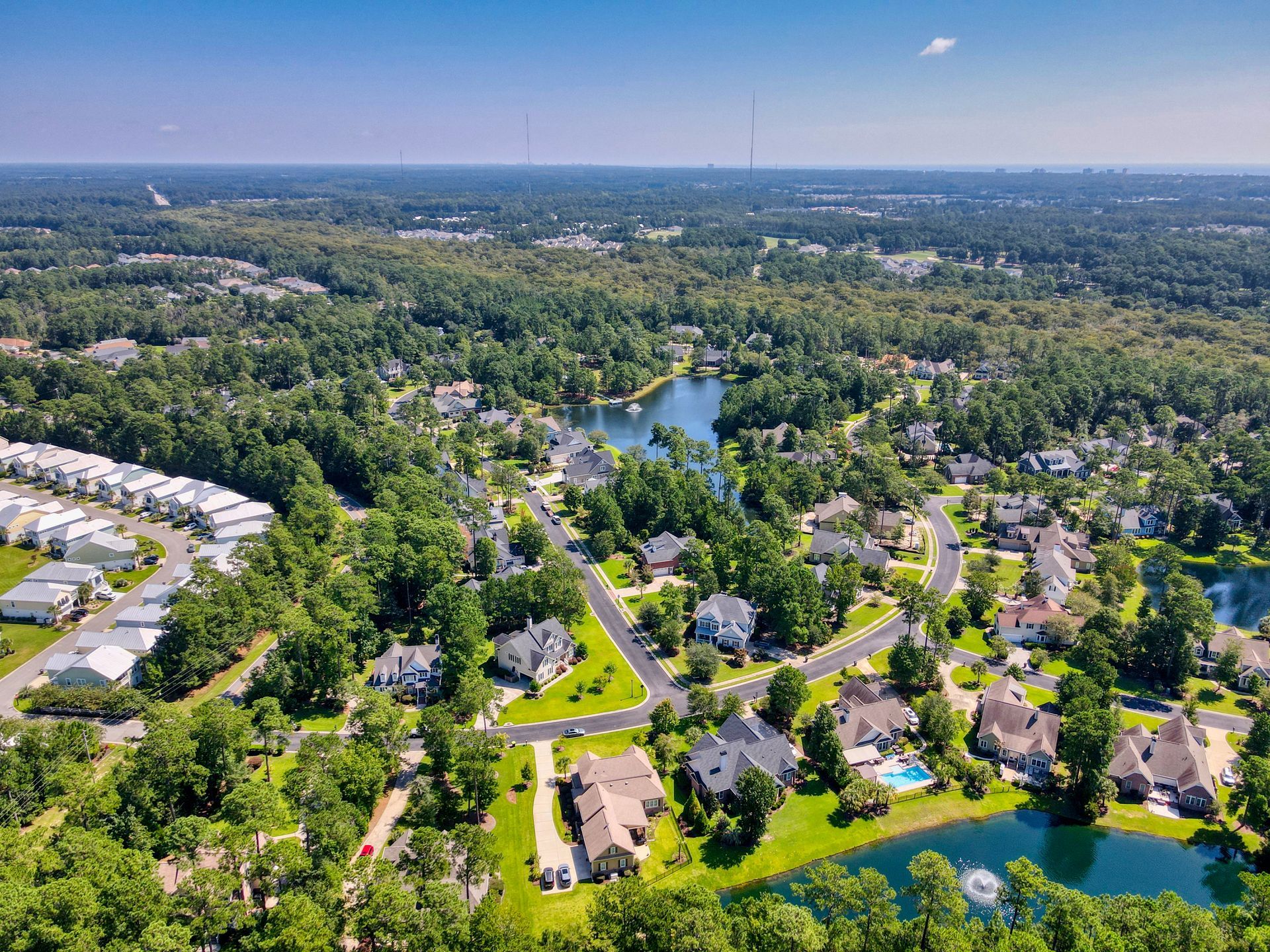 Aerial view of a suburban neighborhood with houses, trees, and lakes on a sunny day.