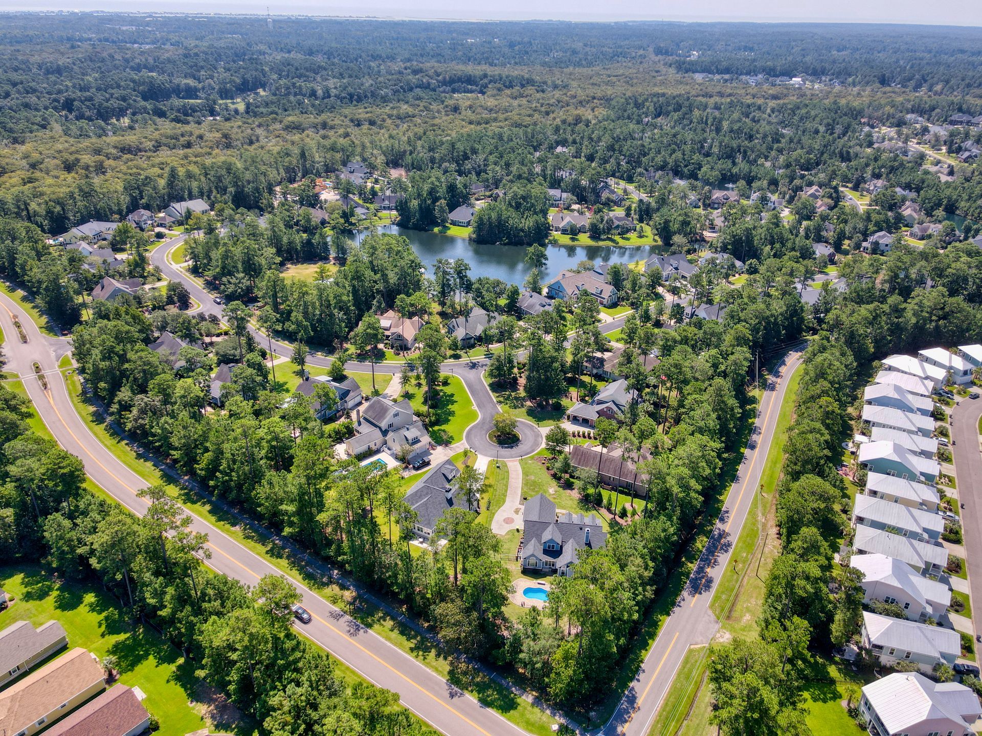 Aerial view of a suburban neighborhood with houses, a lake, trees, and roads.