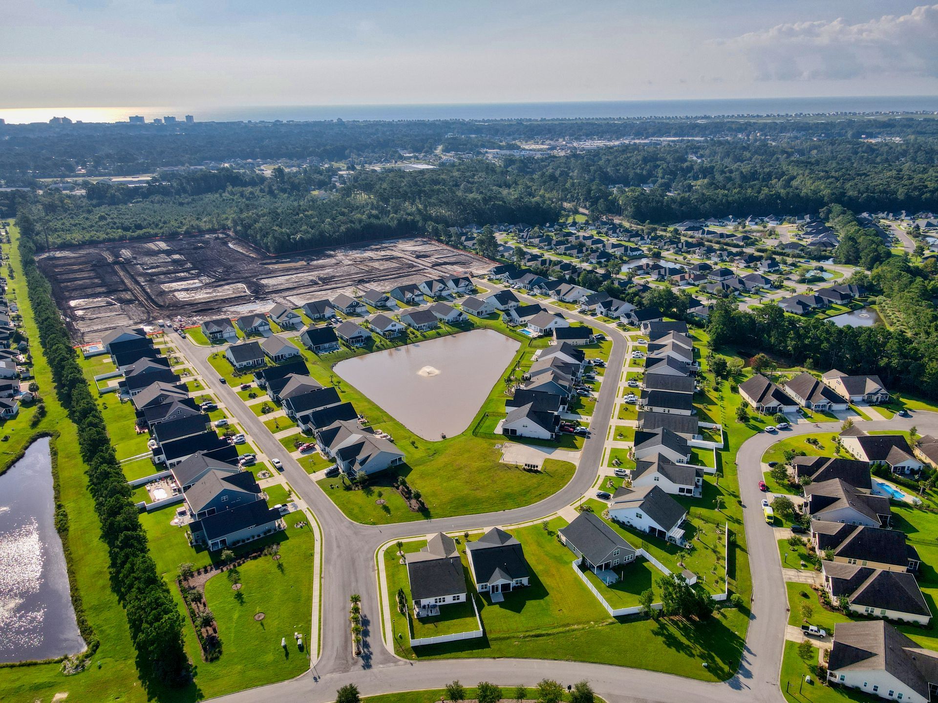 Aerial view of suburban neighborhood with houses, streets, and a pond surrounded by greenery.