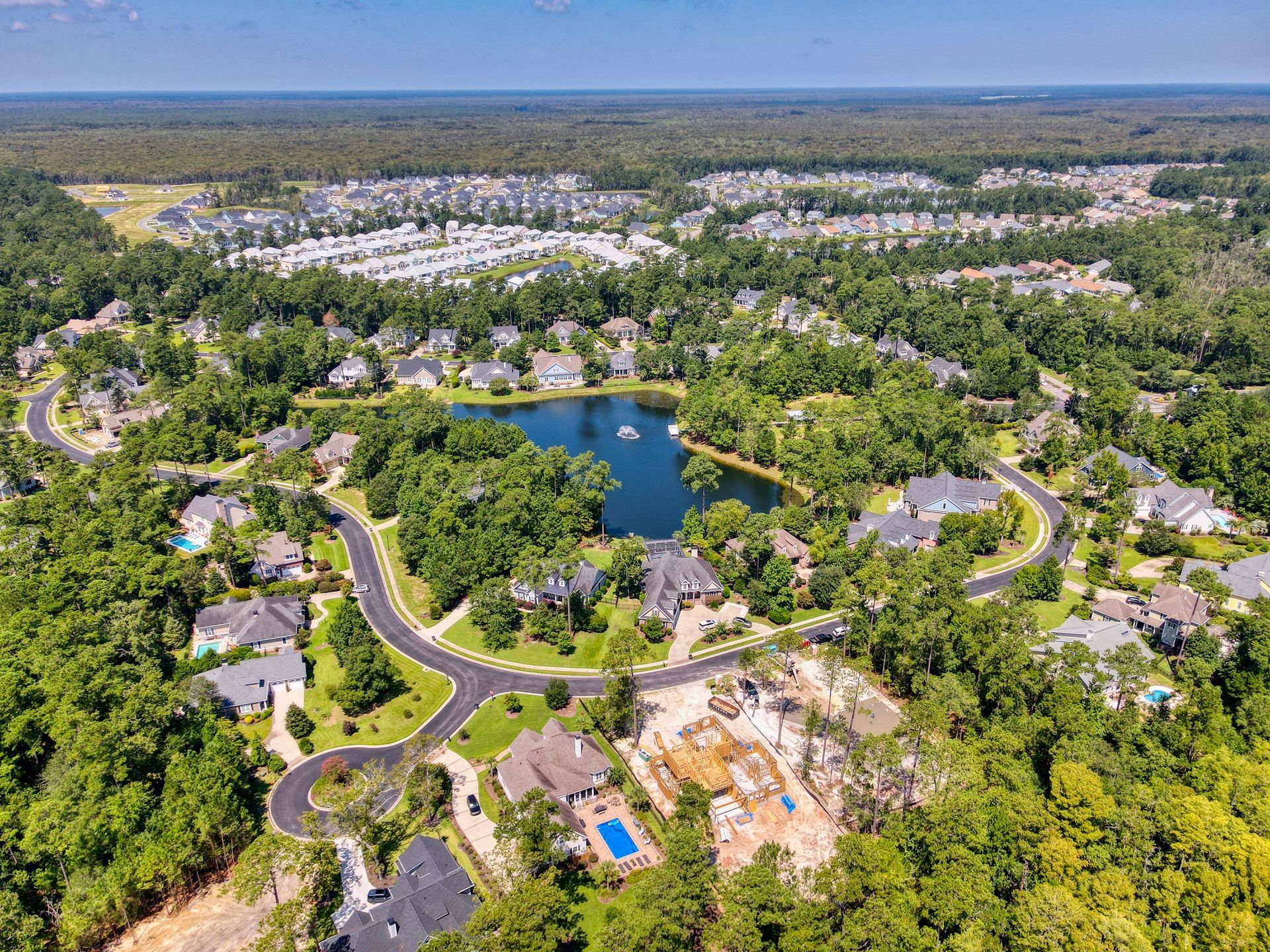 Aerial view of a residential neighborhood with houses, a lake, trees, and roads under a blue sky.