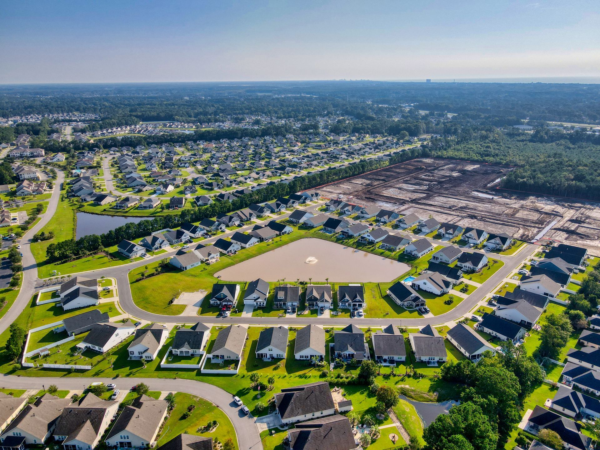 Aerial view of a suburban neighborhood with houses, streets, and undeveloped land.