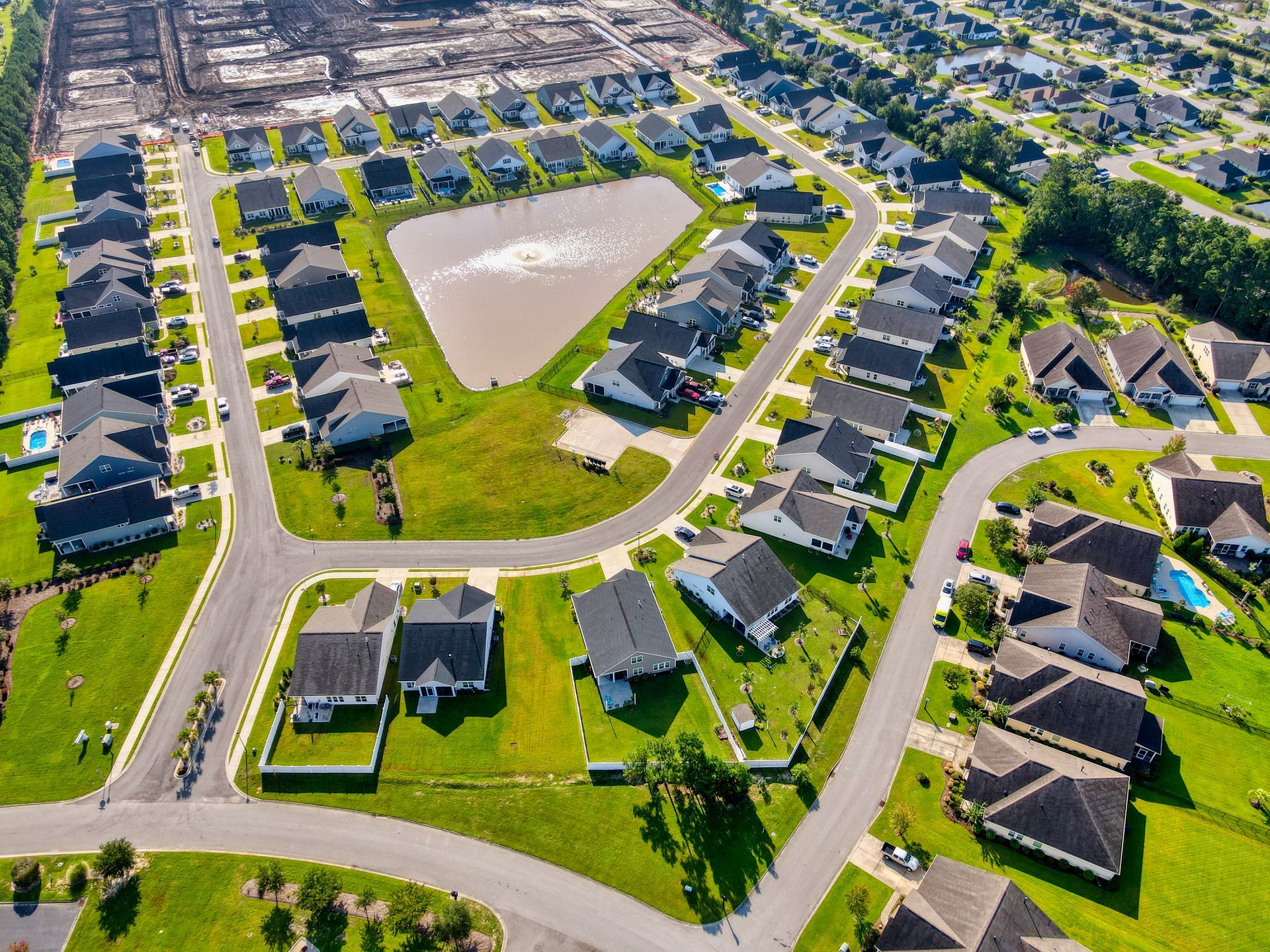 Aerial view of a suburban neighborhood with houses, a pond, and green lawns.