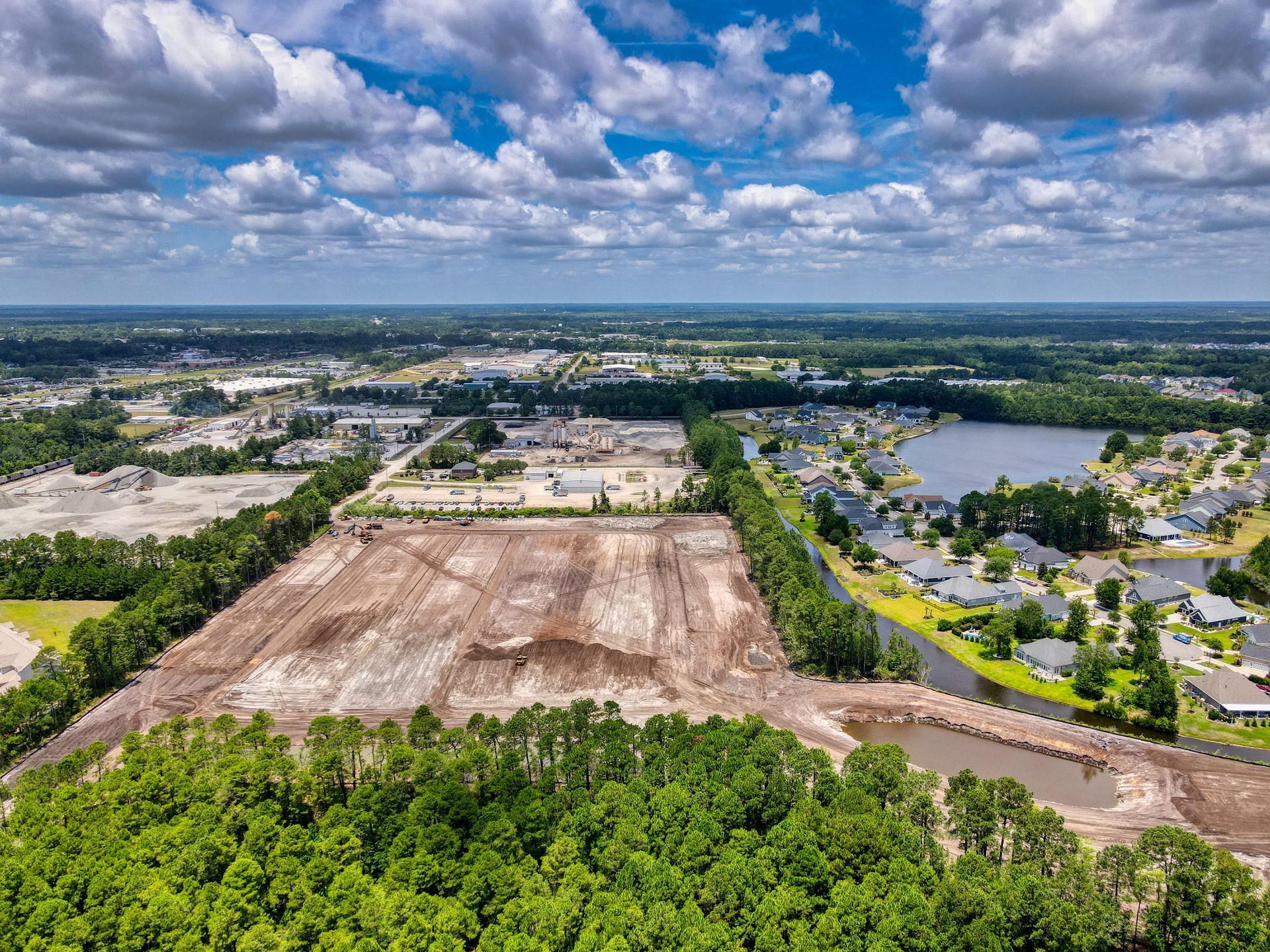 Aerial view of cleared land, trees, and buildings under a cloudy sky.