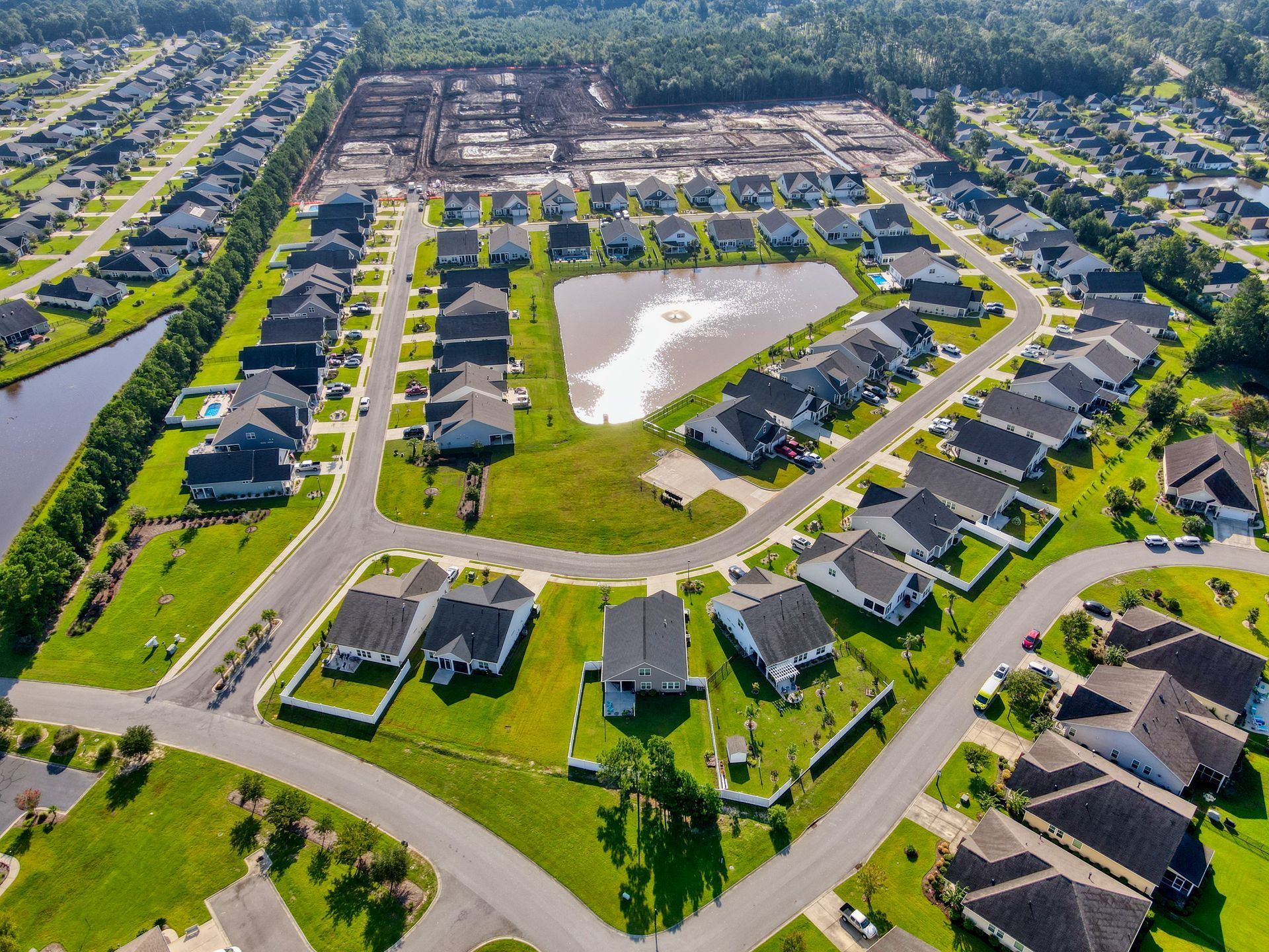 Aerial view of a suburban neighborhood with houses, streets, and a pond under a sunny sky.