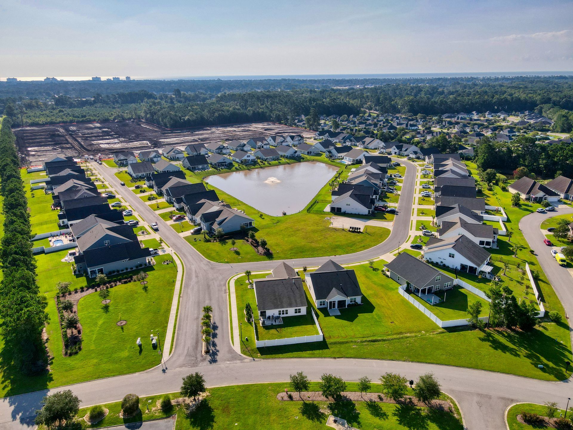 Aerial view of a suburban neighborhood with houses, streets, a pond, and lush green lawns.