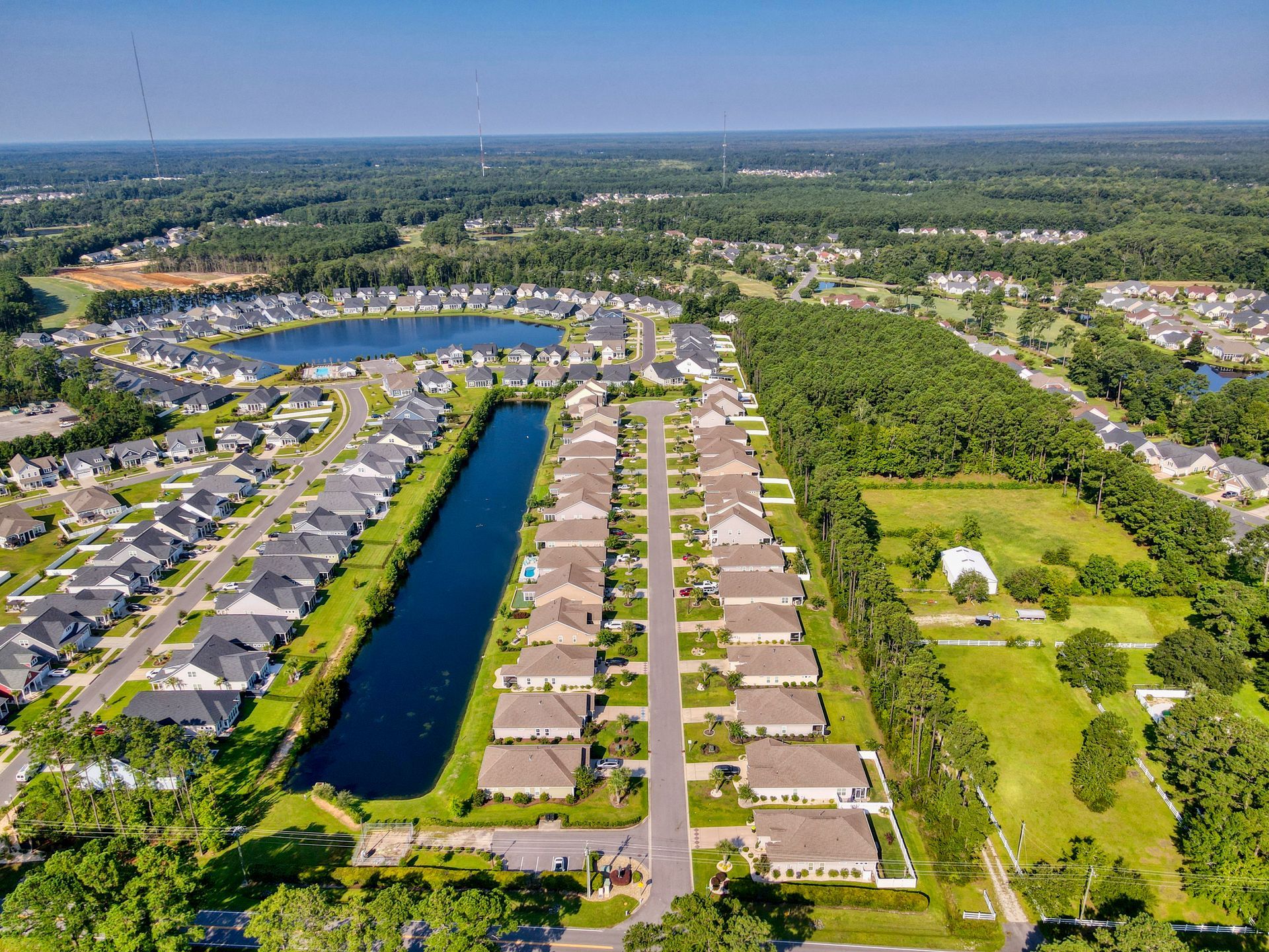 Aerial view of a suburban neighborhood with houses, ponds, and green spaces under a blue sky.