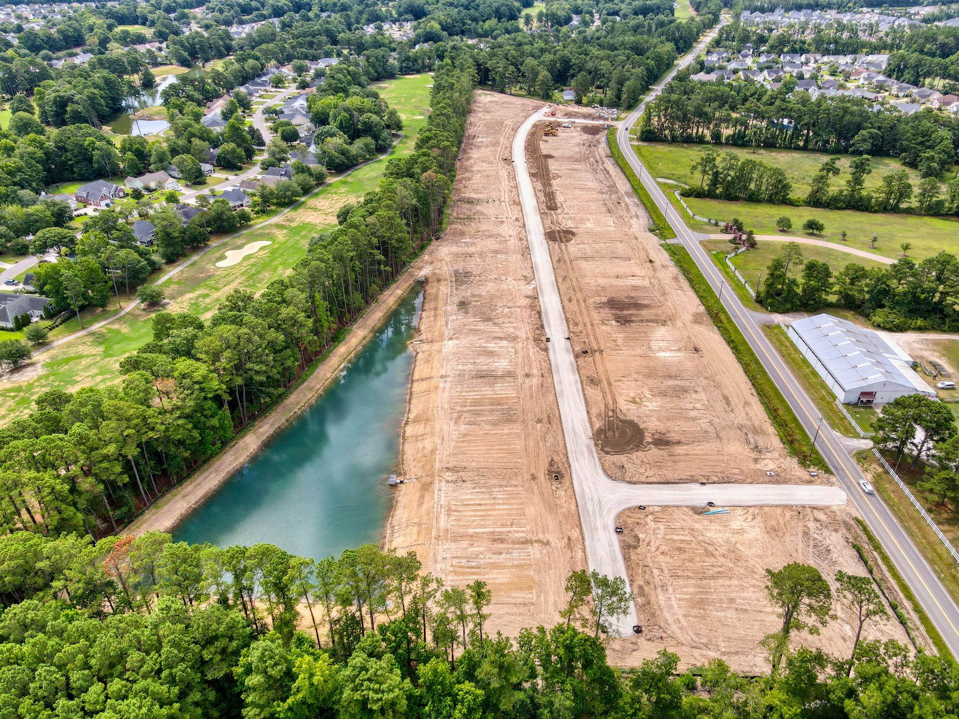 Aerial view of cleared land with roads, a lake, and trees, likely for development.