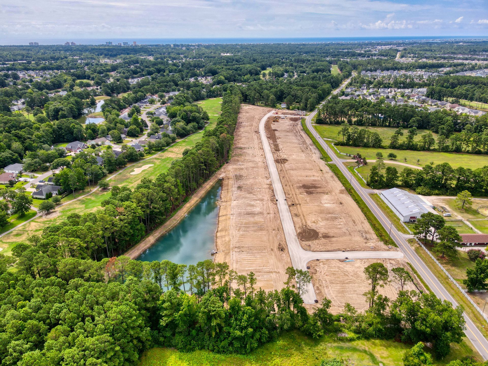 Aerial view of a cleared construction site with graded land, a road, and a retention pond.