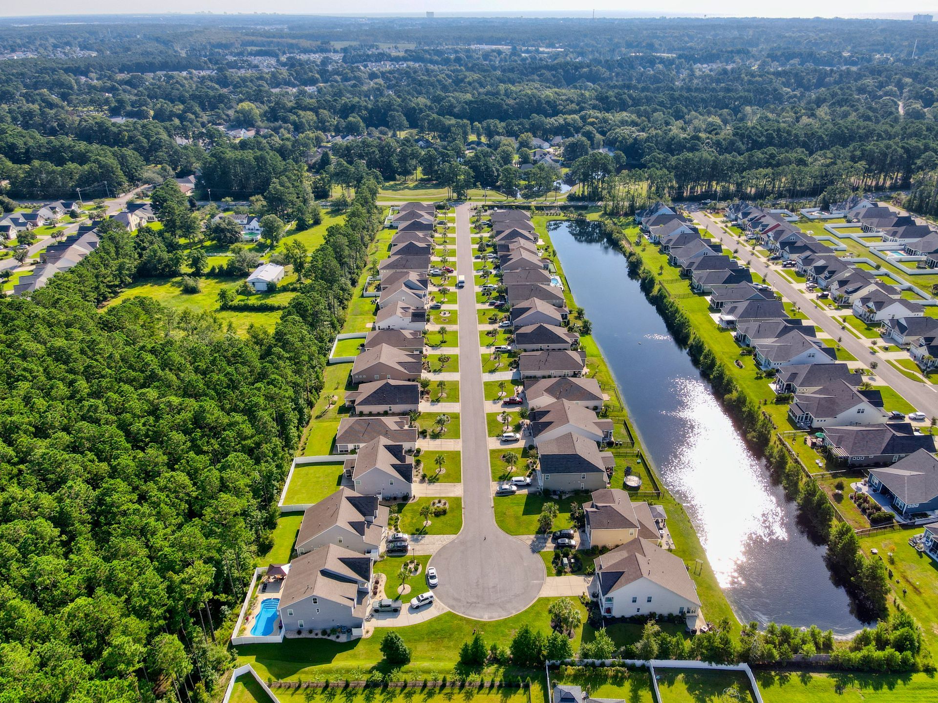 Aerial view of a suburban neighborhood with rows of houses, a pond, and surrounding trees.