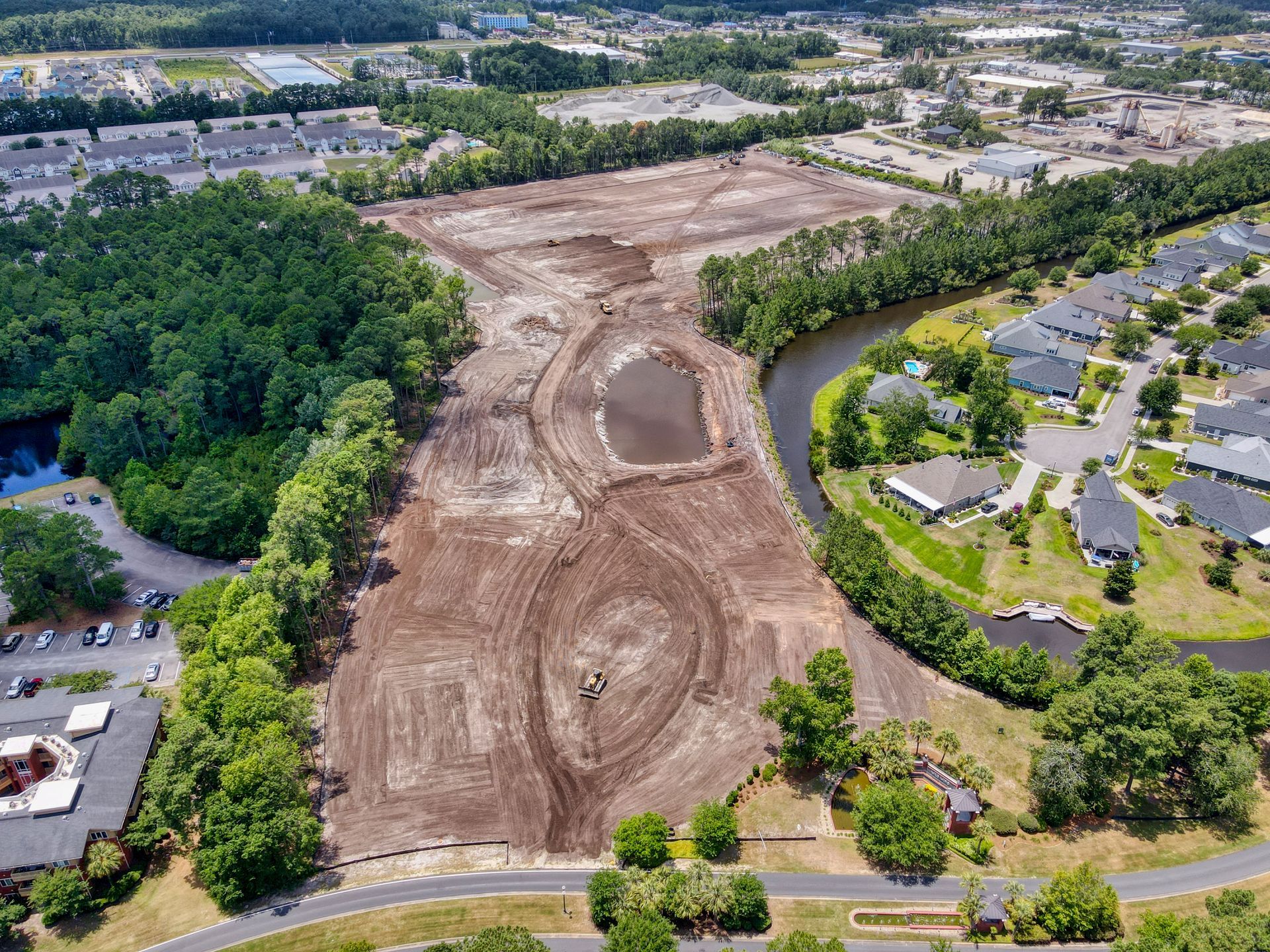 Aerial view of cleared land, next to a river and residential neighborhood; construction site.