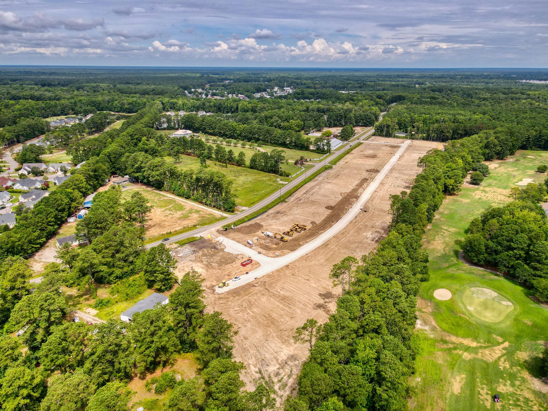 Aerial view of cleared land, surrounded by trees, with some structures visible.