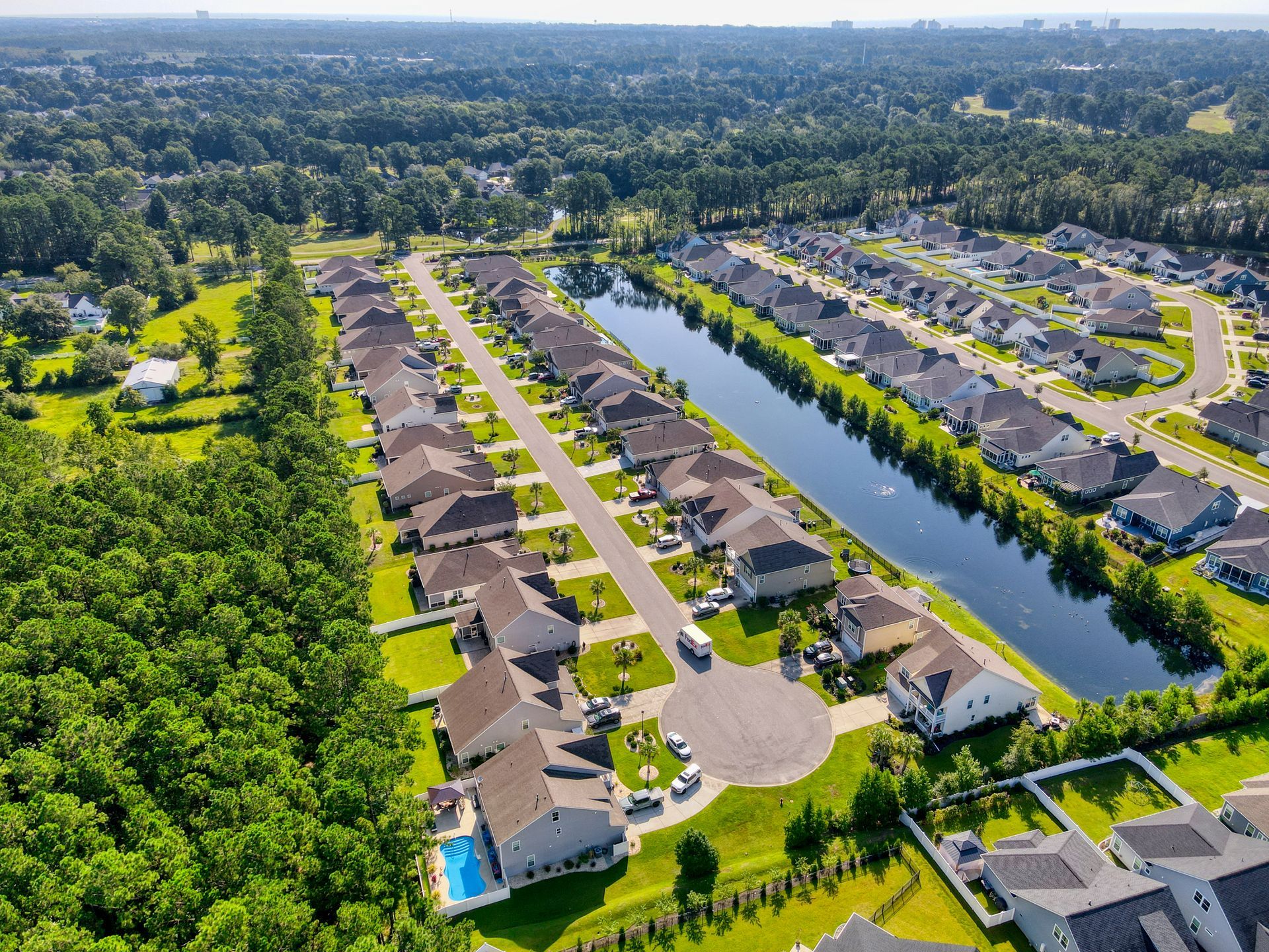 Aerial view of a suburban neighborhood with rows of houses, a lake, and surrounding trees.