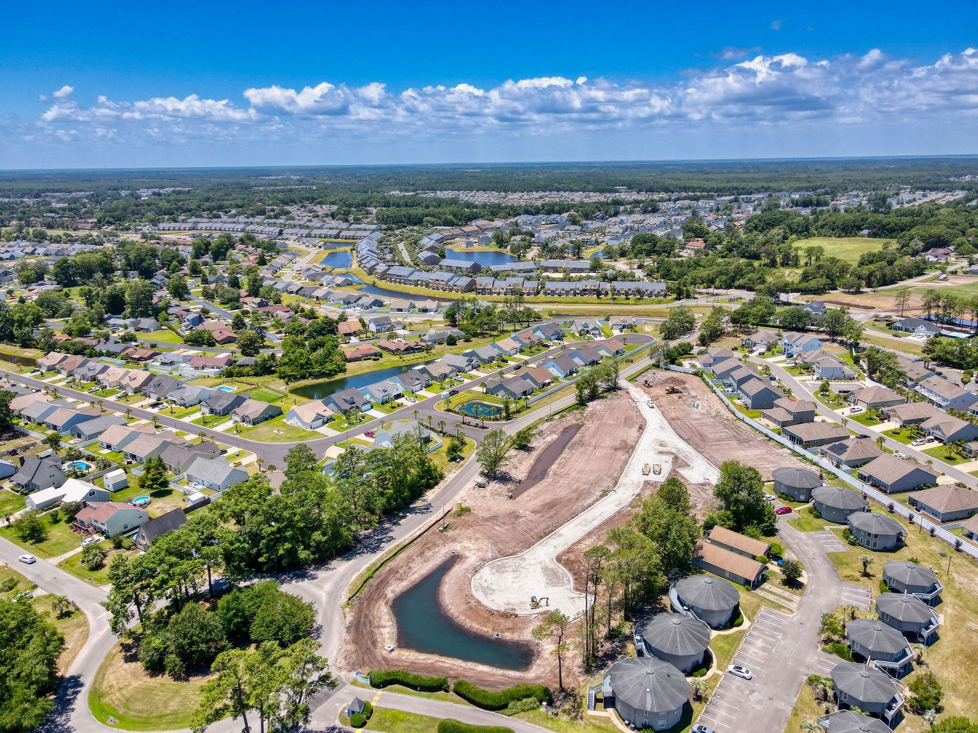Aerial view of a suburban neighborhood with houses, ponds, and construction. Blue sky with clouds overhead.