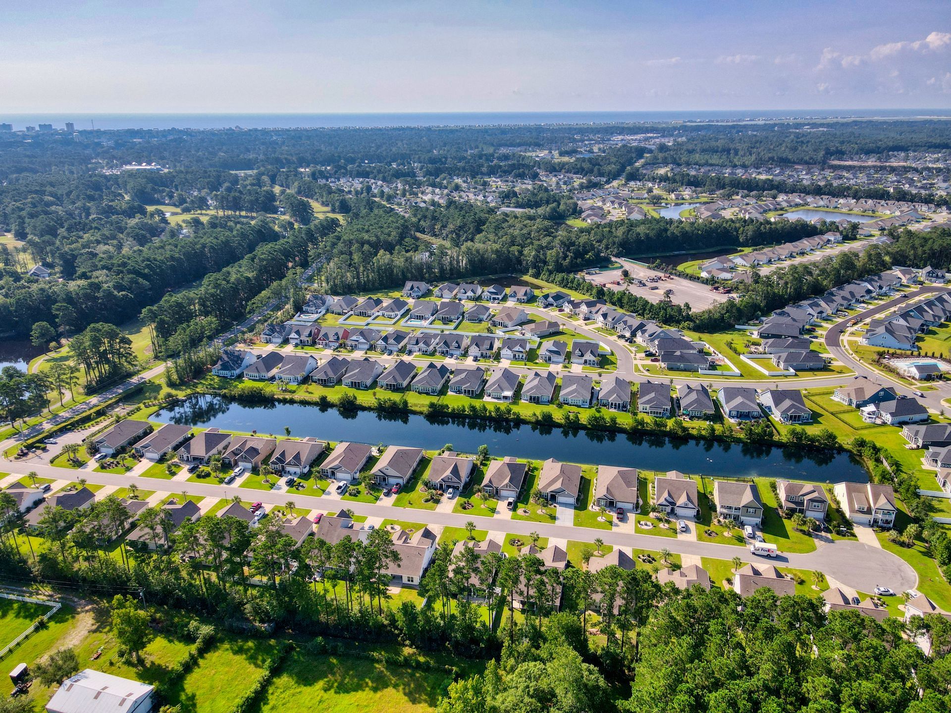Aerial view of a residential neighborhood with houses, a lake, trees, and blue sky.