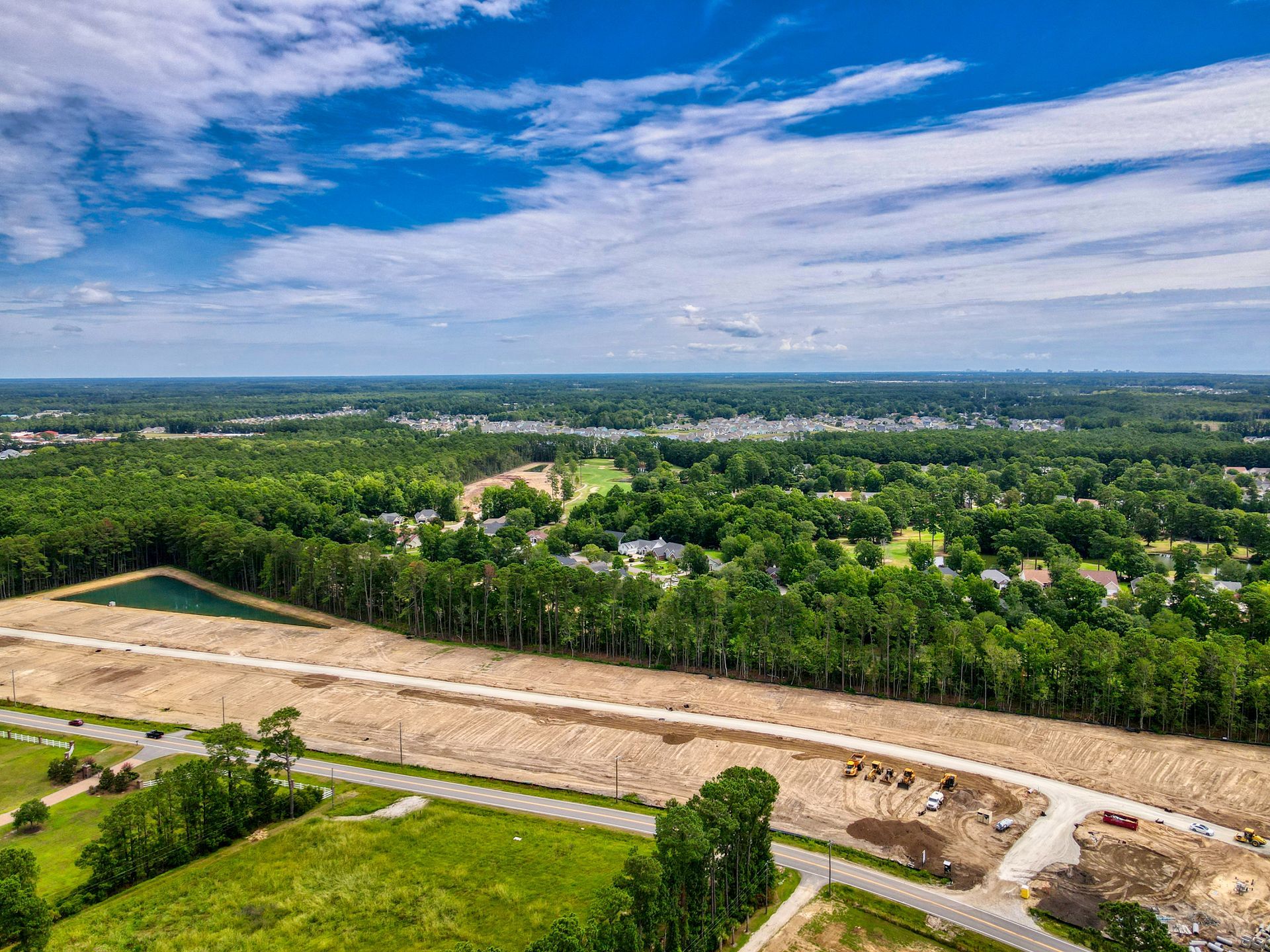 Aerial view of cleared land for development with a green treeline, blue sky.