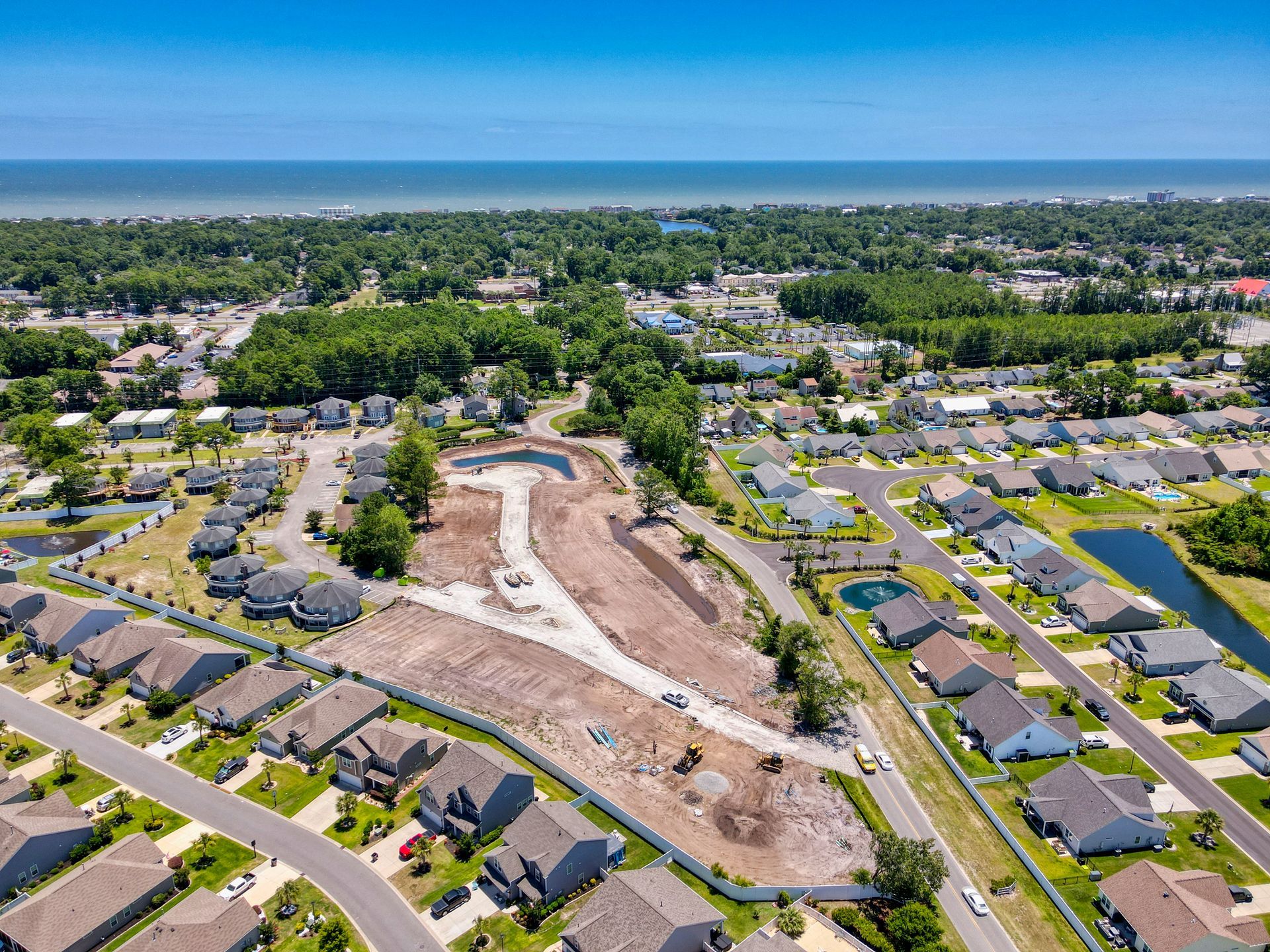 Aerial view of new construction, with a partially built residential area and a coastal backdrop.
