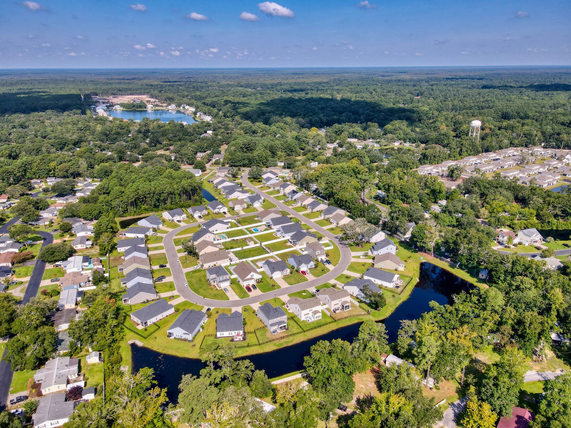 Aerial view of a suburban neighborhood surrounded by green trees and a small lake with houses and a cul-de-sac.