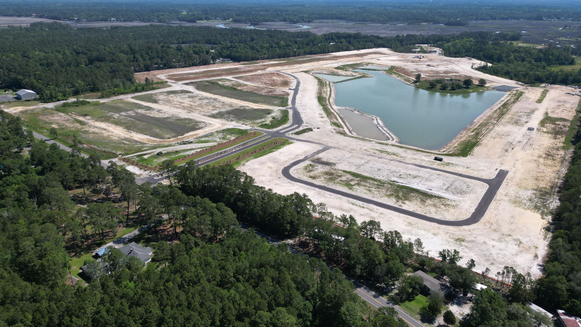 Aerial view of a cleared construction site with roads, a lake, and surrounding trees.