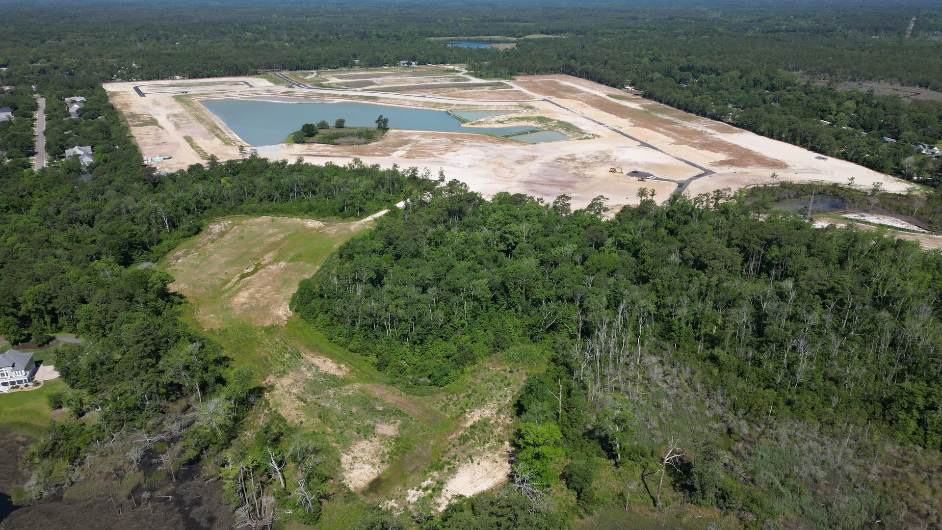 Construction site clearing land near a forest, with dirt patches, a lake, and surrounding trees.