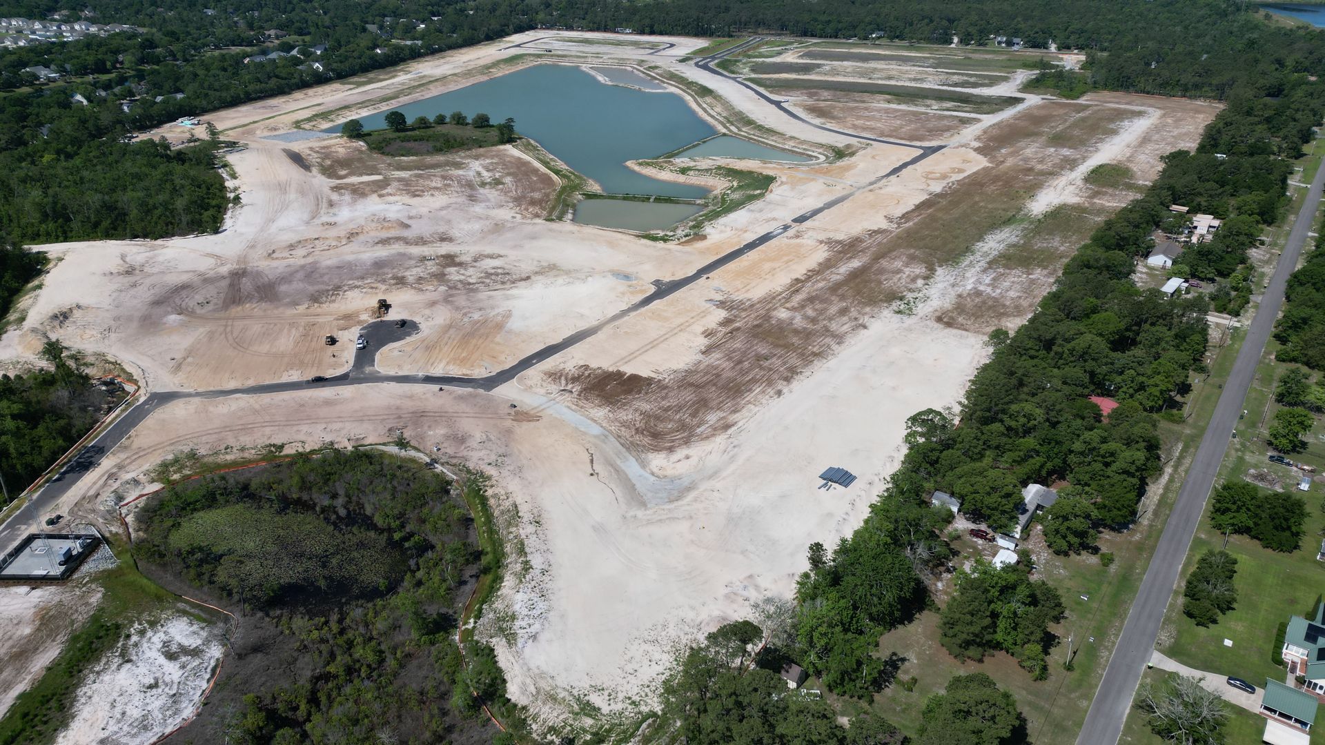 Aerial view of a cleared construction site with a pond and access roads.