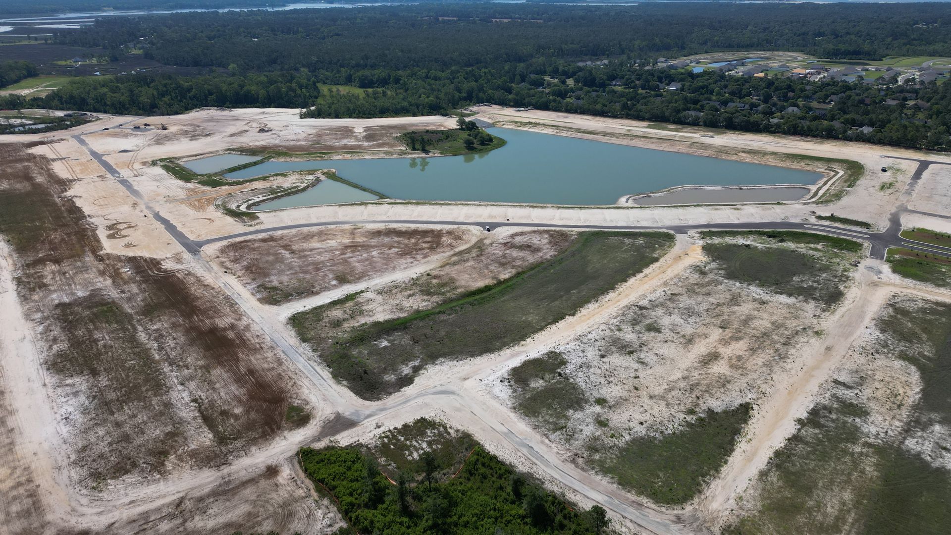Aerial view of a cleared construction site with a pond and roads.