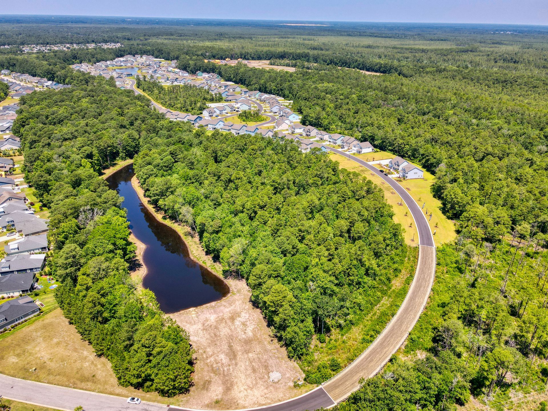 Aerial view of a residential neighborhood with a winding road, lake, and surrounding forest.