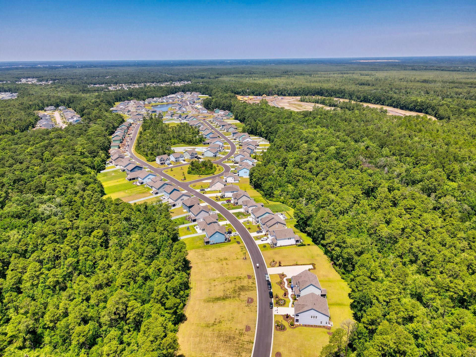 Aerial view of a suburban neighborhood with houses lining curved roads, surrounded by dense green forest.
