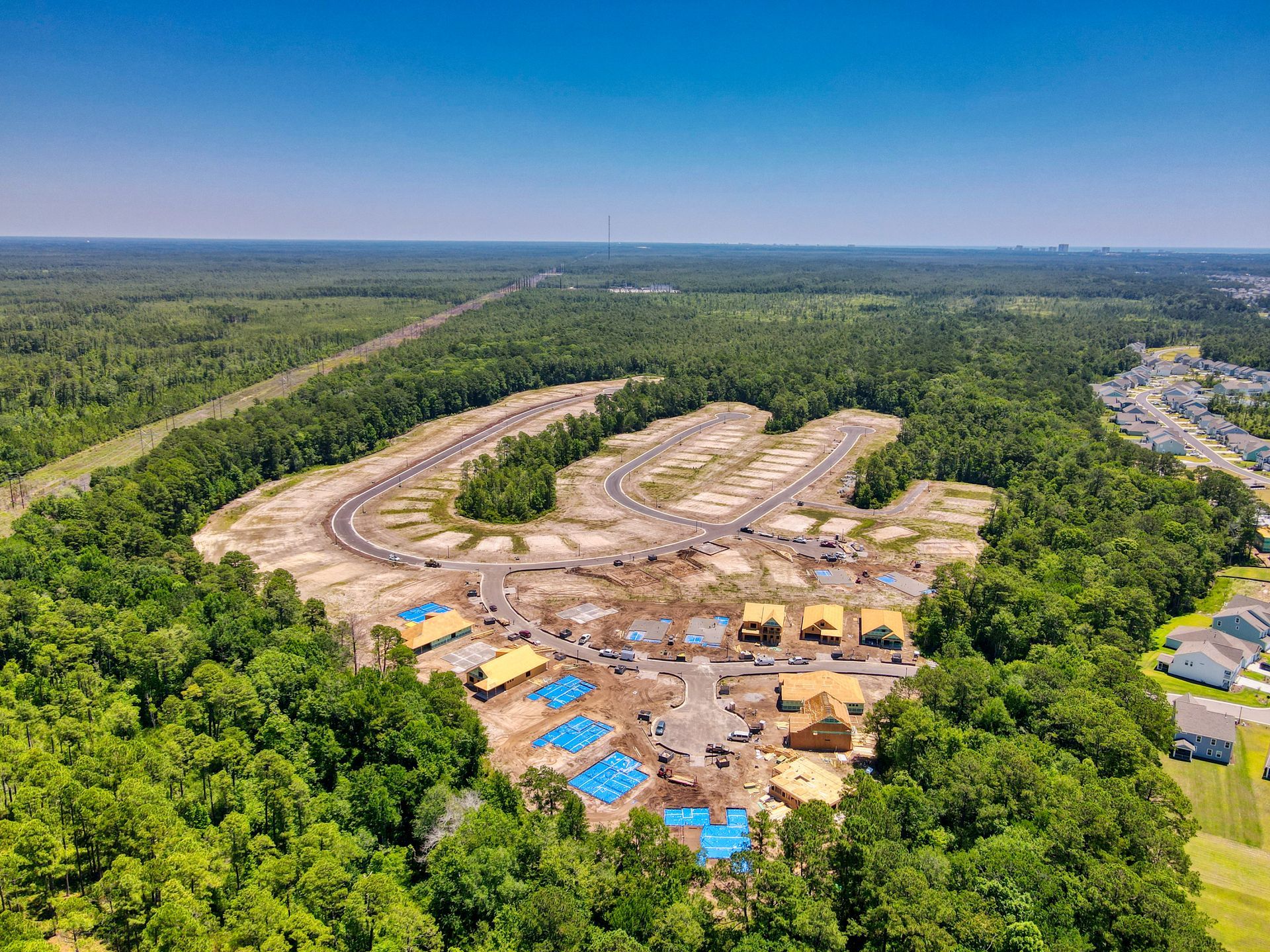 Aerial view of a new housing development under construction in a wooded area. Unfinished homes and roadways visible.