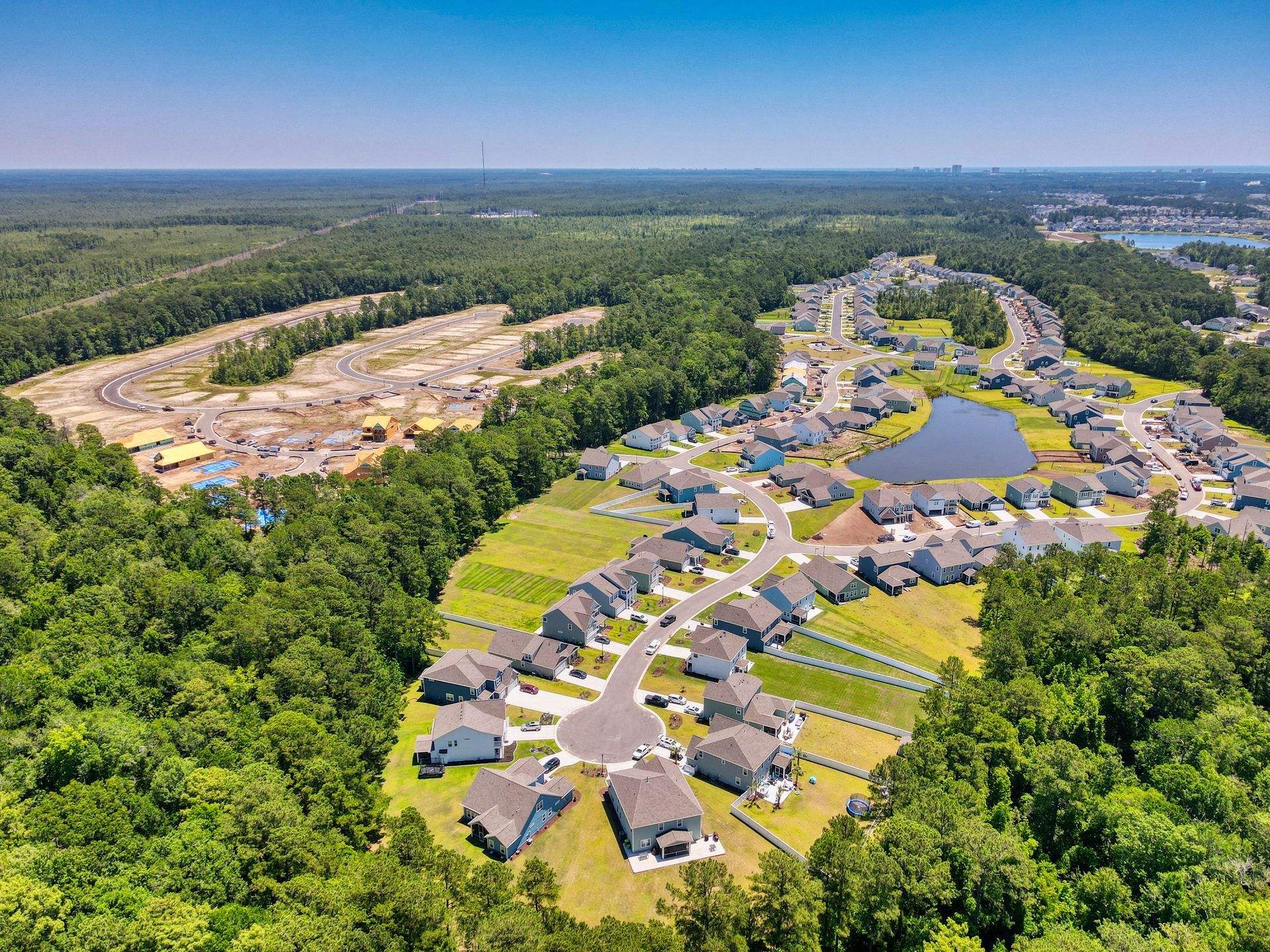 Aerial view of a residential neighborhood with houses, a lake, and a construction site surrounded by trees.