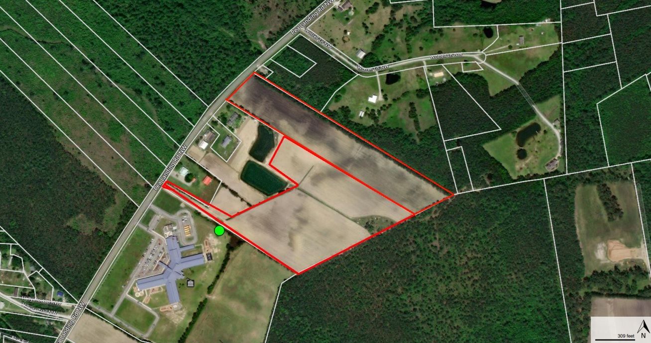 Aerial view of farmland bordered by roads and forest, outlined in red. Light and dark brown fields.