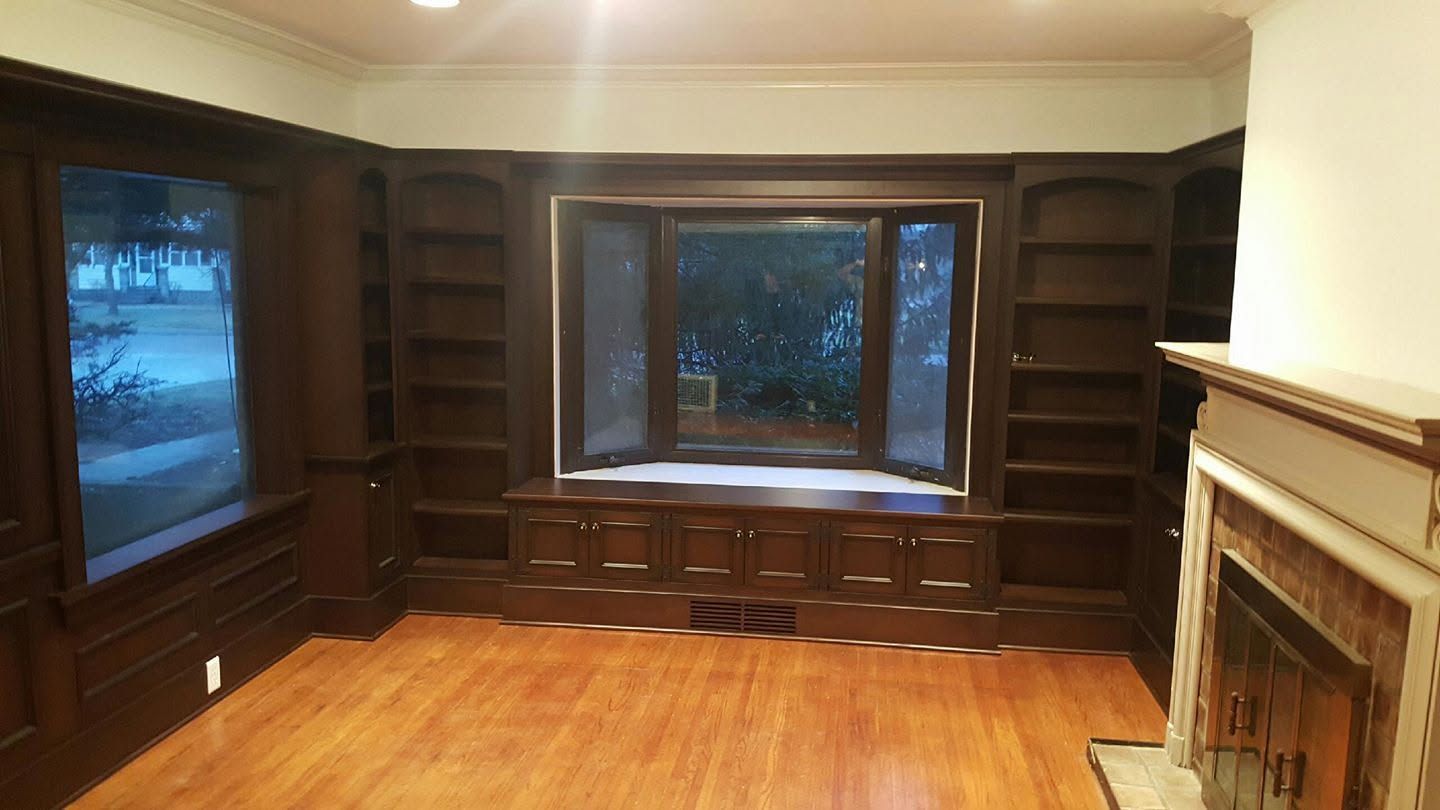 Empty living room with dark built-in shelves, a bay window, hardwood floor, and a fireplace