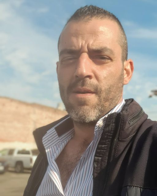 A man with a beard is wearing a black jacket and striped shirt