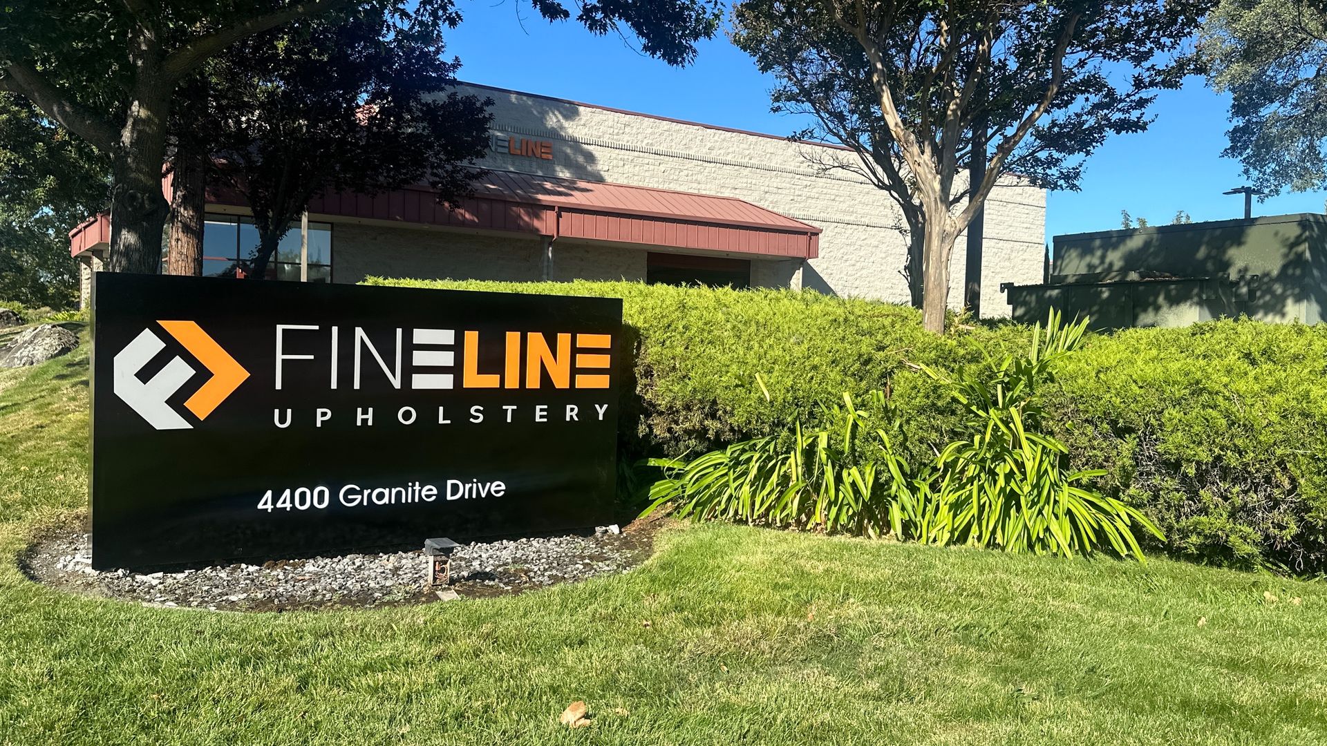 Sign for Fine Line Upholstery at 4400 Granite Drive, with logo on a grassy lawn, building in the background.