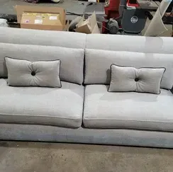 A white couch with two pillows on it is sitting on a concrete floor.