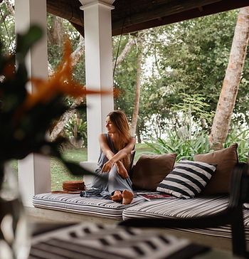 A woman is sitting on a couch on a porch with a laptop.