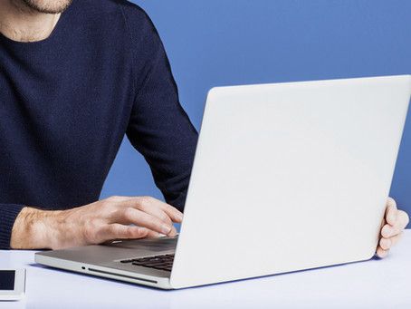 A man in a blue sweater is typing on a laptop