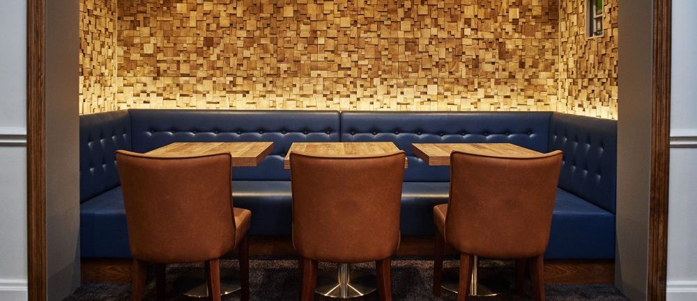 Cozy restaurant booth with brown chairs, blue booth seating, and a wood block wall.