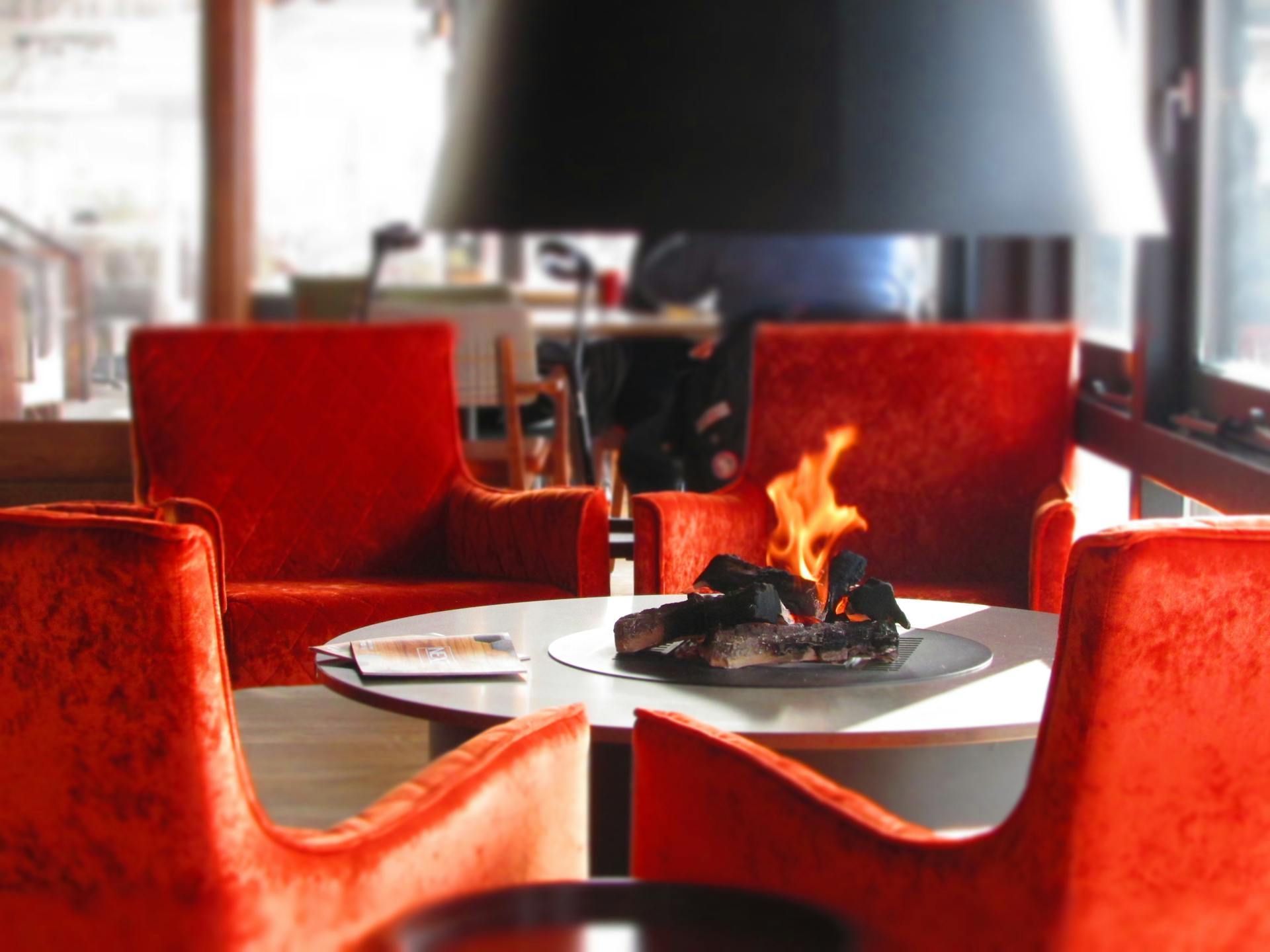 Four red velvet chairs around a small table with a burning fire pit.