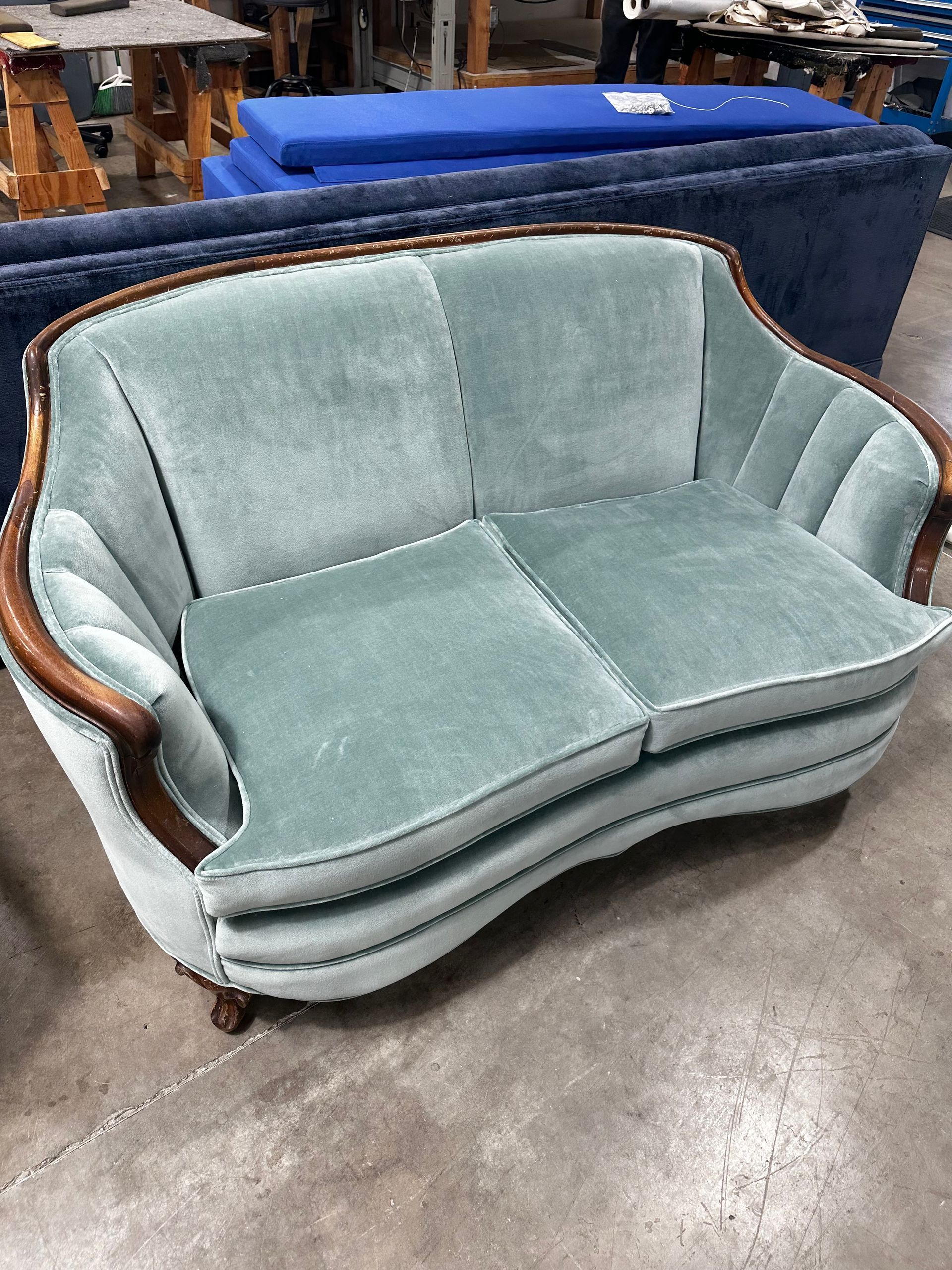 A blue couch is sitting on a concrete floor in a warehouse.