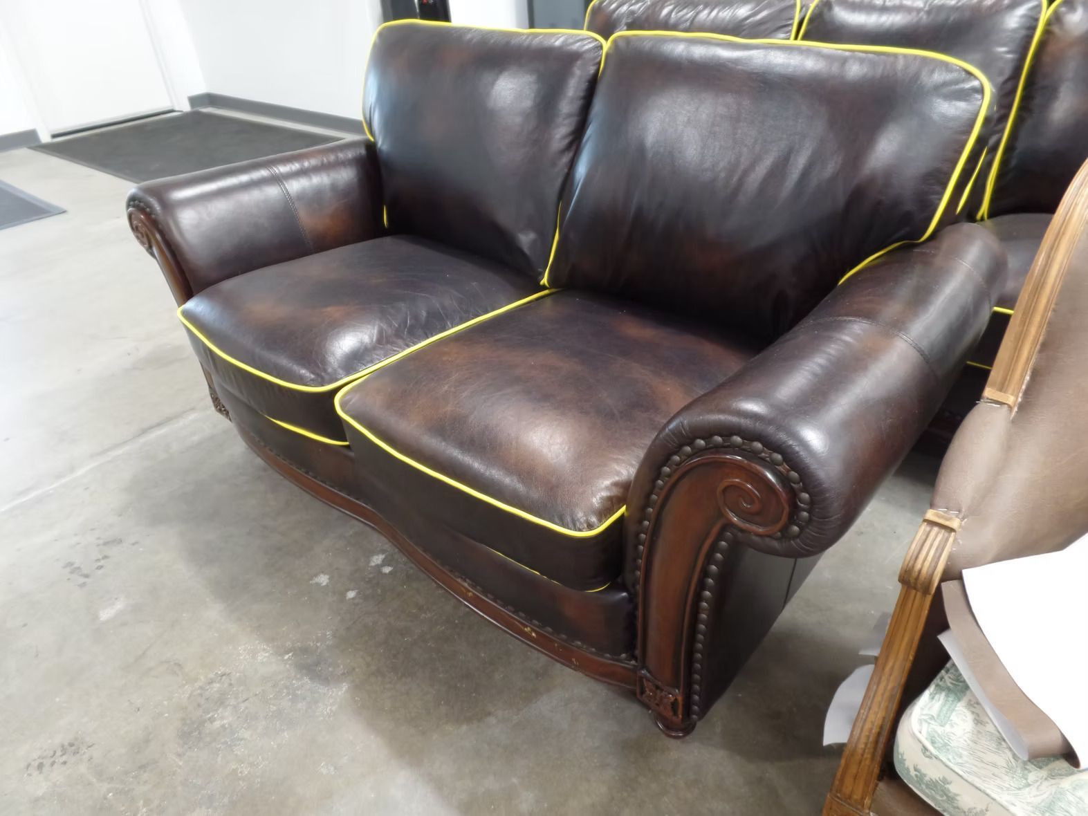 A brown leather couch with yellow trim sits on a concrete floor