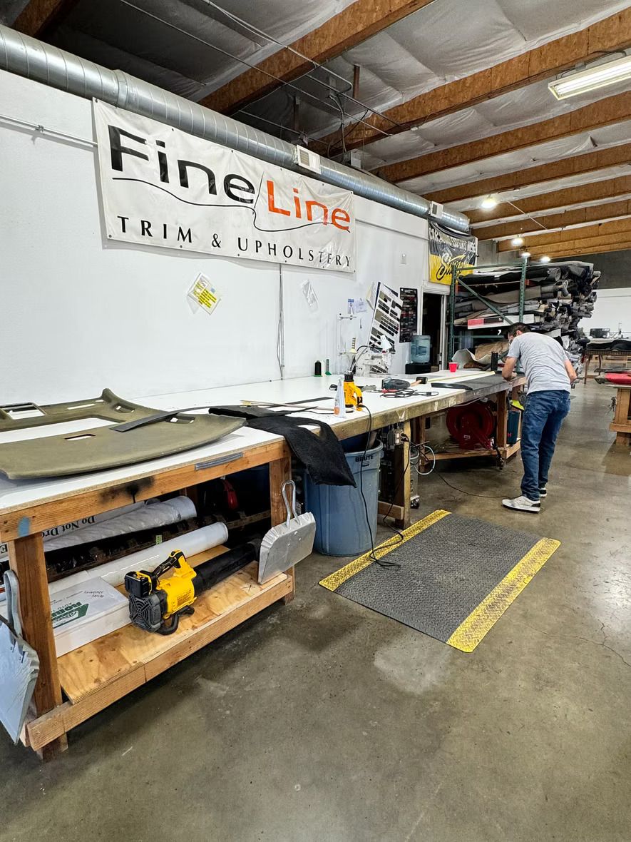 A man is standing in a room with a sign that says `` fineline trim & upholstery ''.