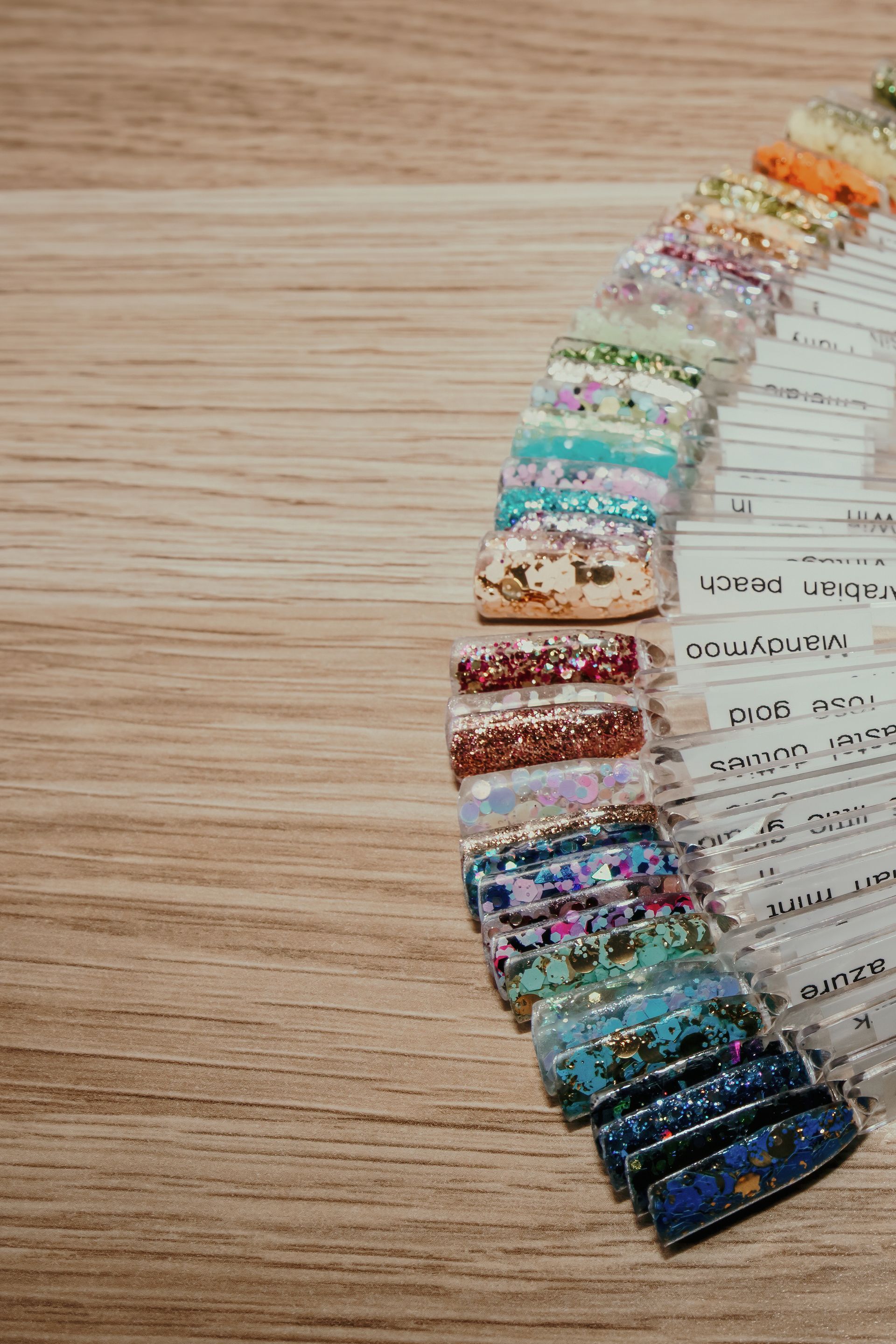Nail polish colour swatches in various glittery shades arranged on a wooden surface. — Admire Skincare and Beauty in Taree, NSW