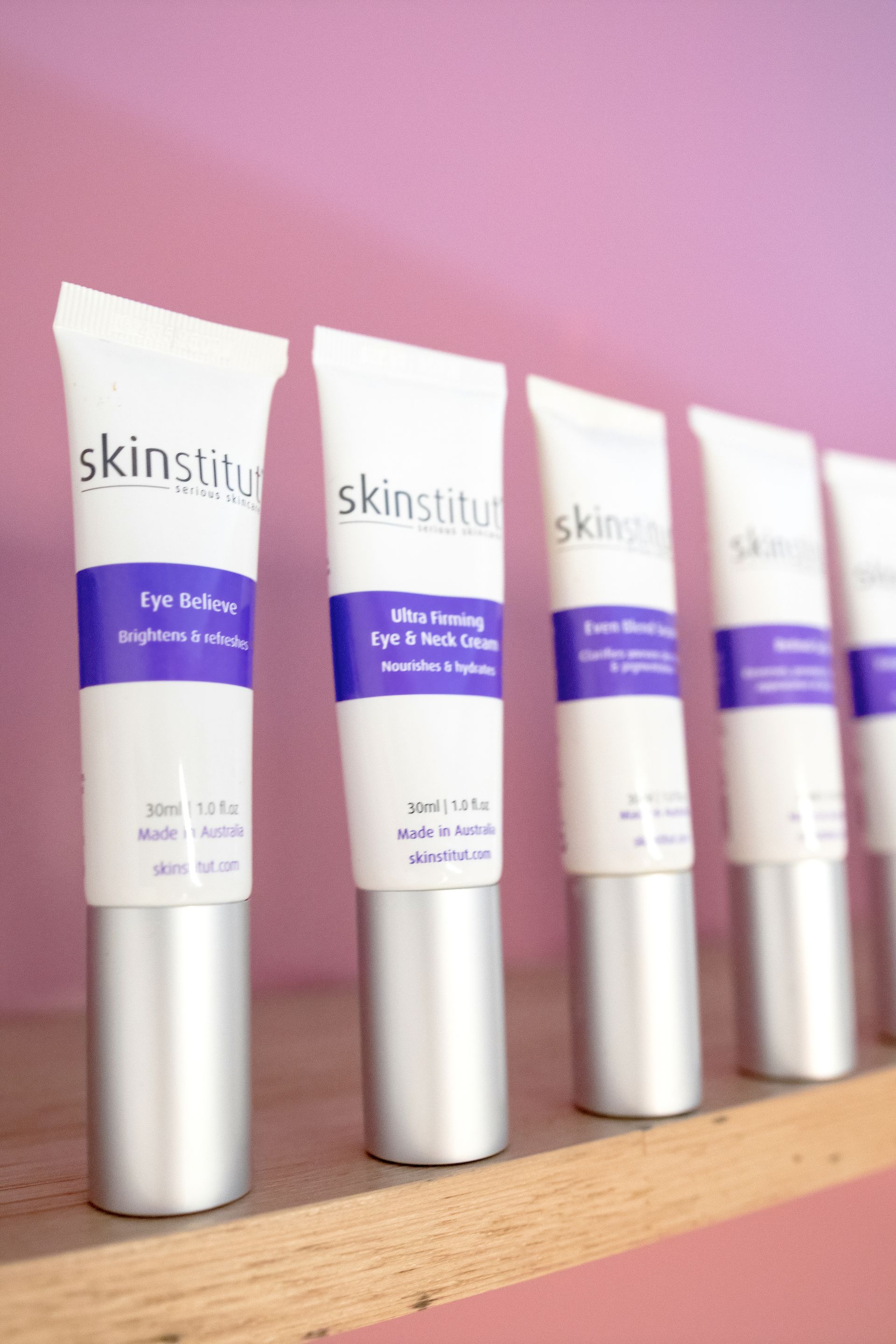 White skincare tubes with purple accents lined up on a shelf, against a pink wall. — Admire Skincare and Beauty in Taree, NSW