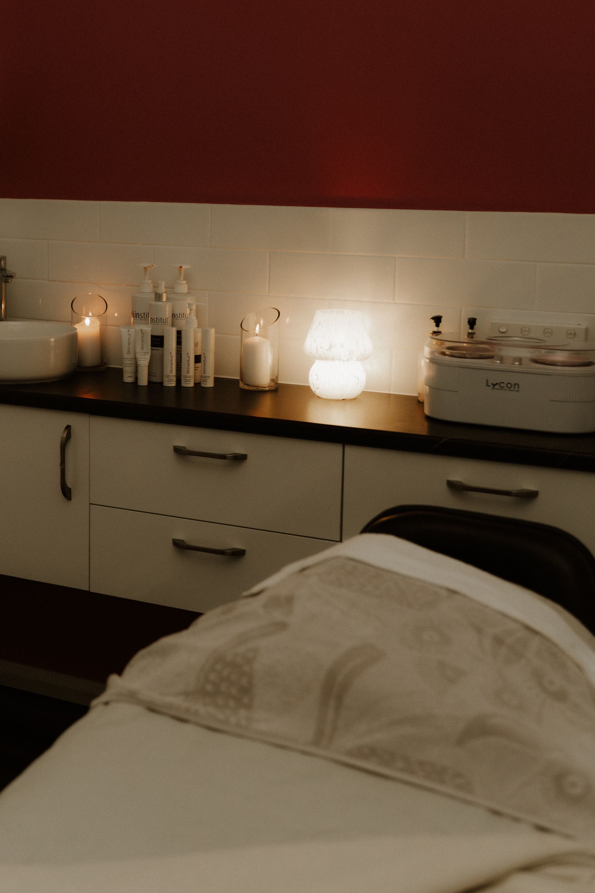 Massage table in spa room, lit by candles and a lamp, with skin care products on a countertop. — Admire Skincare and Beauty in Taree, NSW