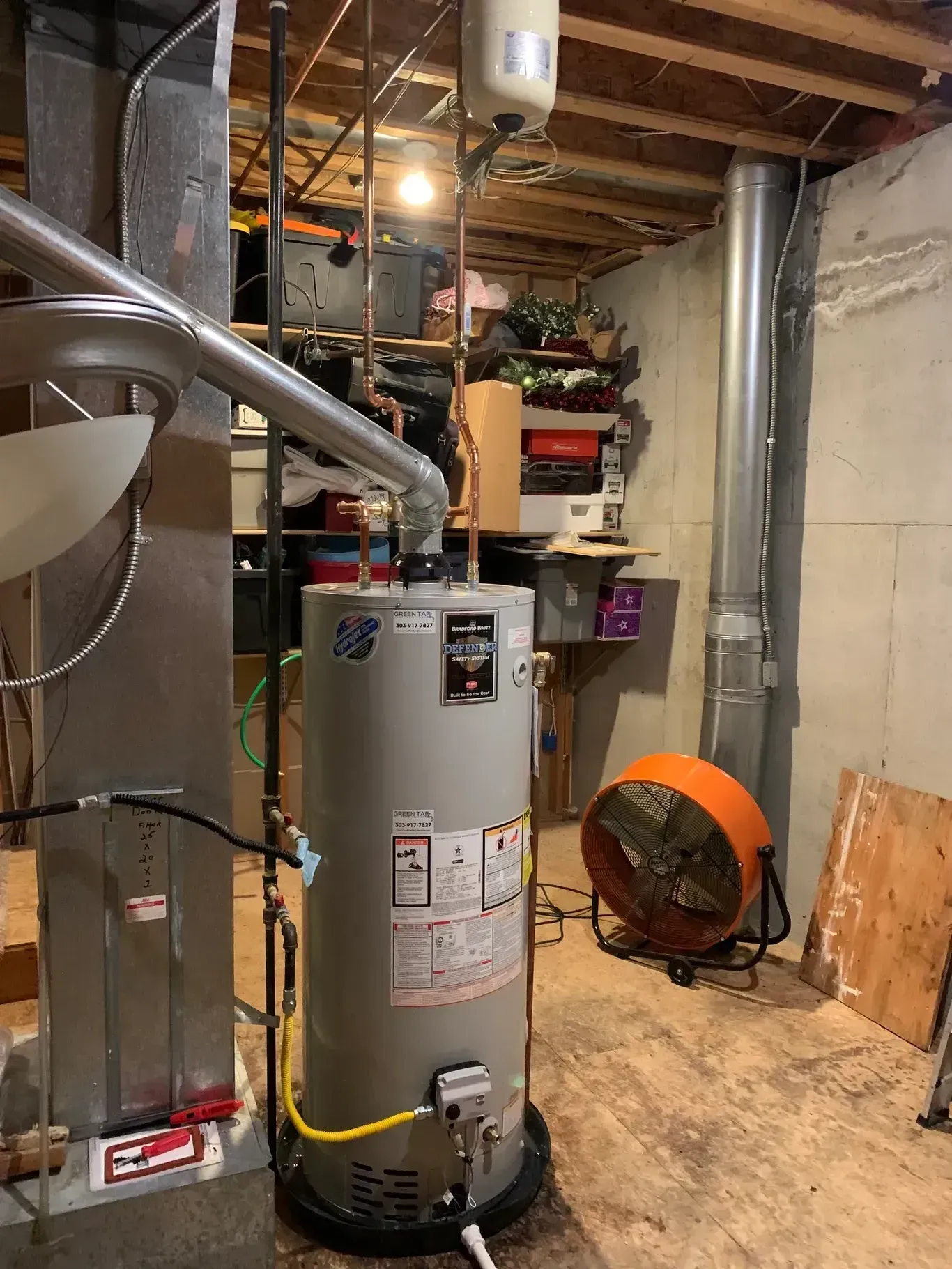 Water heater in a basement with furnace, vent pipe, and a space heater.