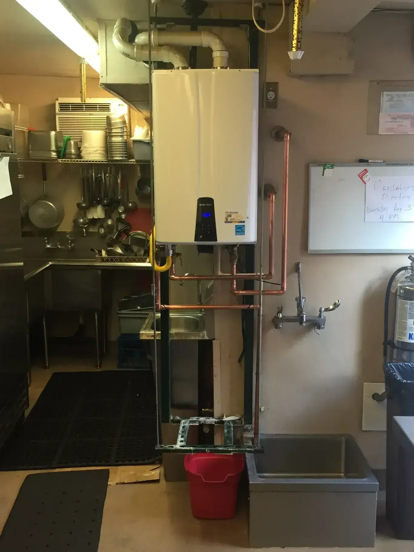 Water heater with copper pipes, sink, and red trash can in a commercial kitchen setting.